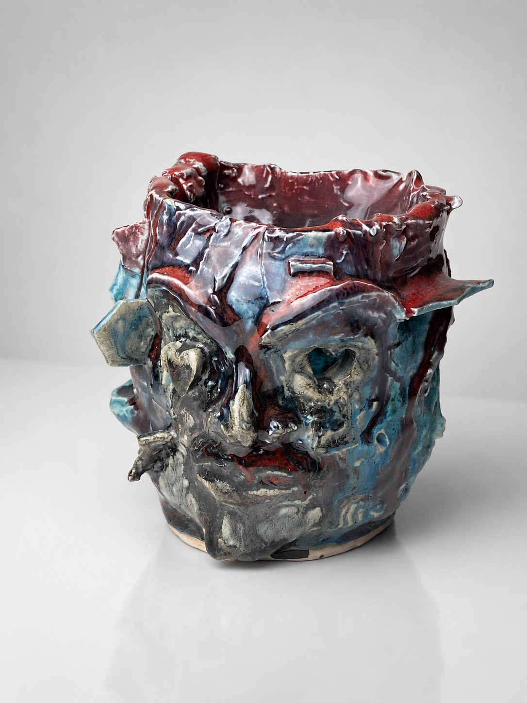 A ceramic art piece resembling a distorted human face with exaggerated features, painted in red, blue, black, and metallic colors.