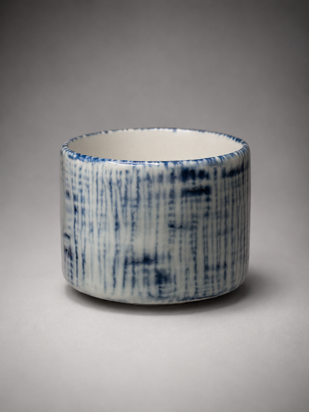 Blue and white ceramic cup with vertical lines pattern on a gray background.