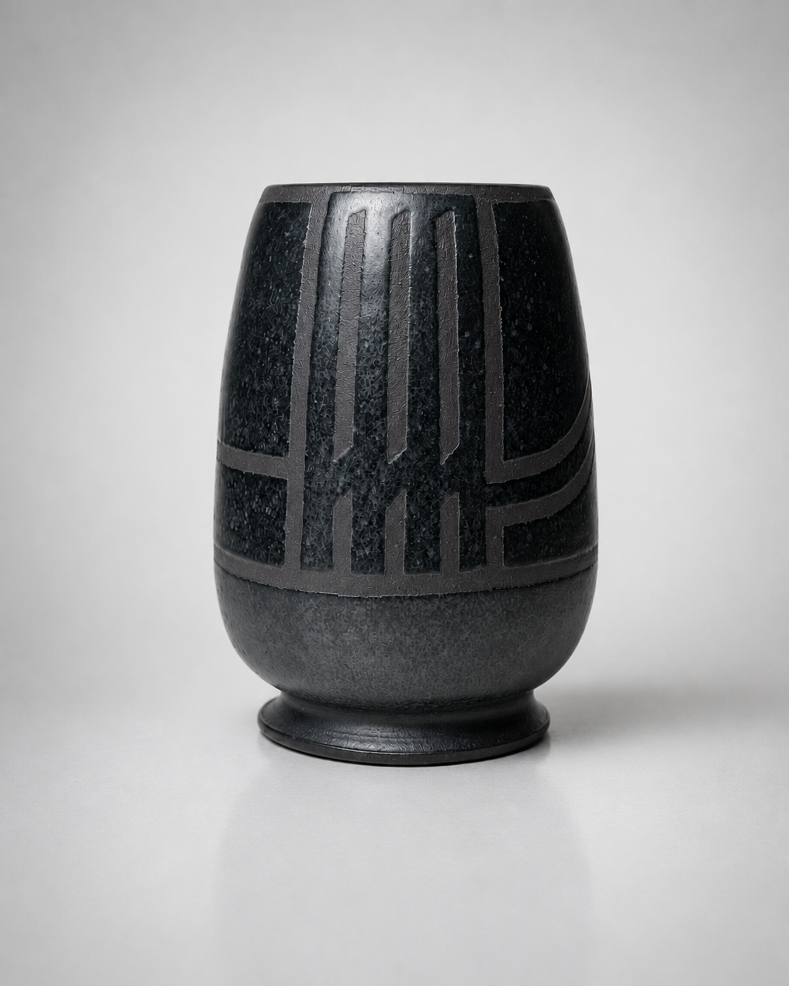 Black ceramic vase with geometric patterns, placed on a flat surface against a plain light gray background.