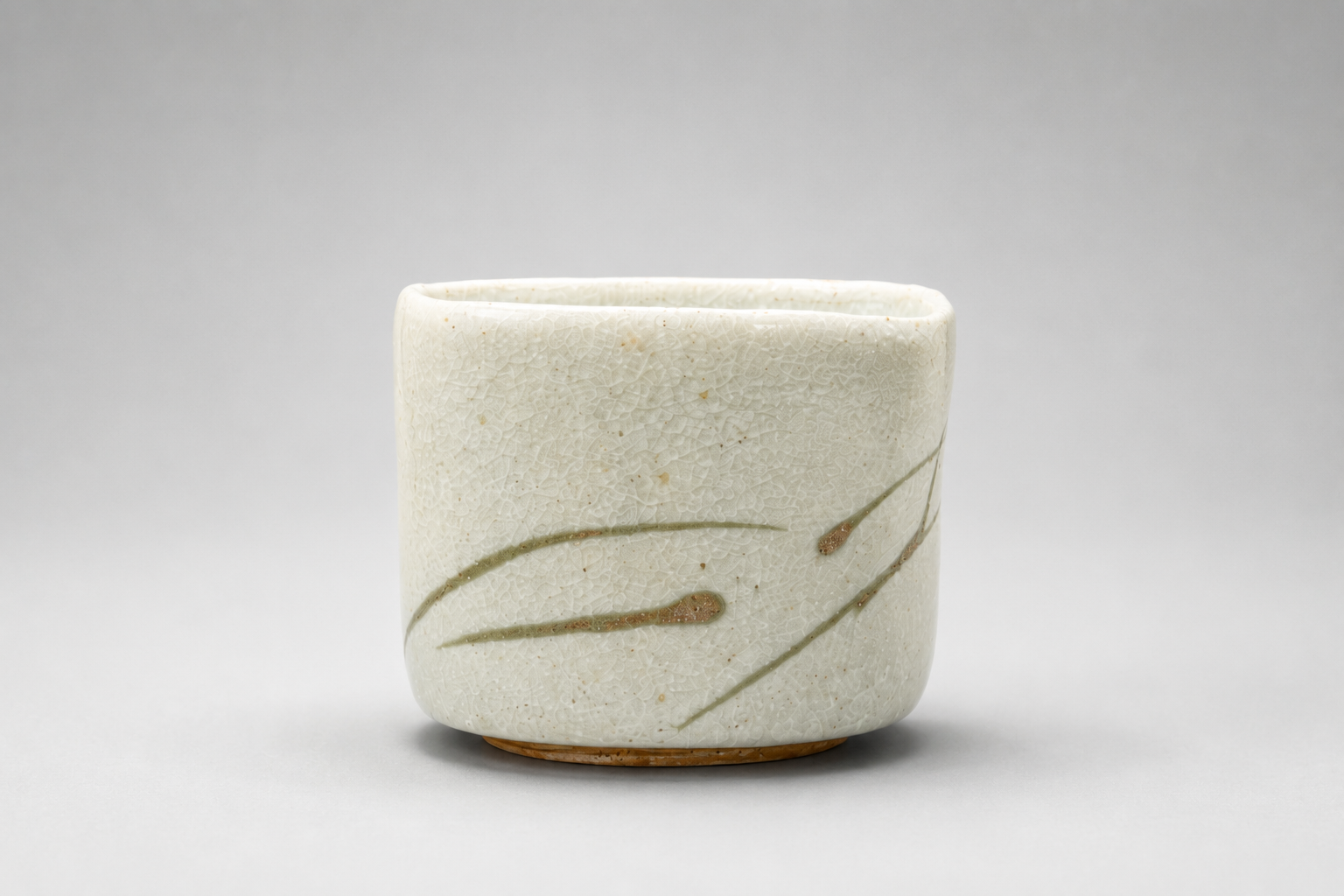 White ceramic cup with subtle crackle glaze and simple green and brown brushstroke design, set against a plain gray background.