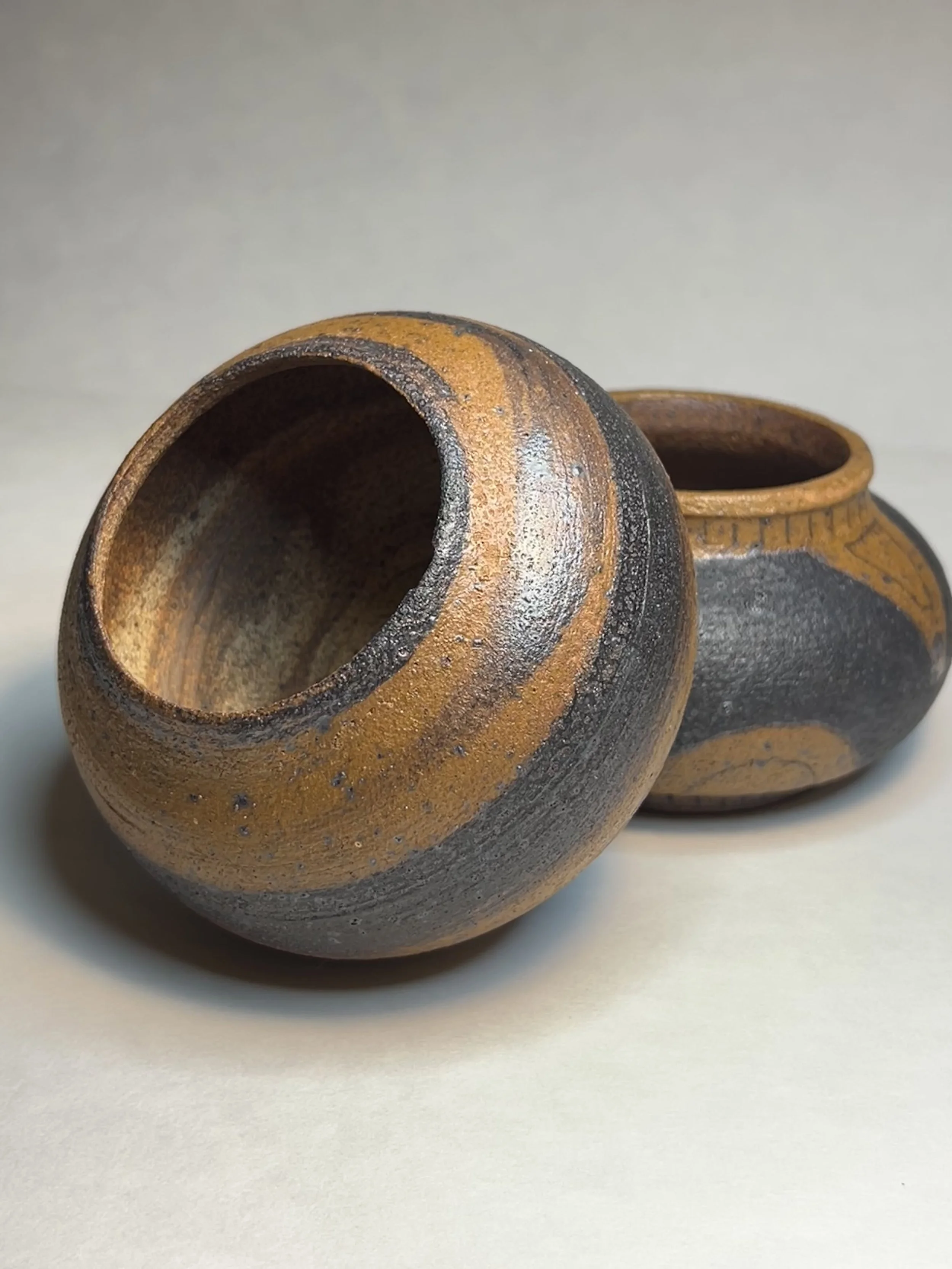 Close-up of two small, handmade clay pots with a textured, earthy appearance, placed on a plain surface.