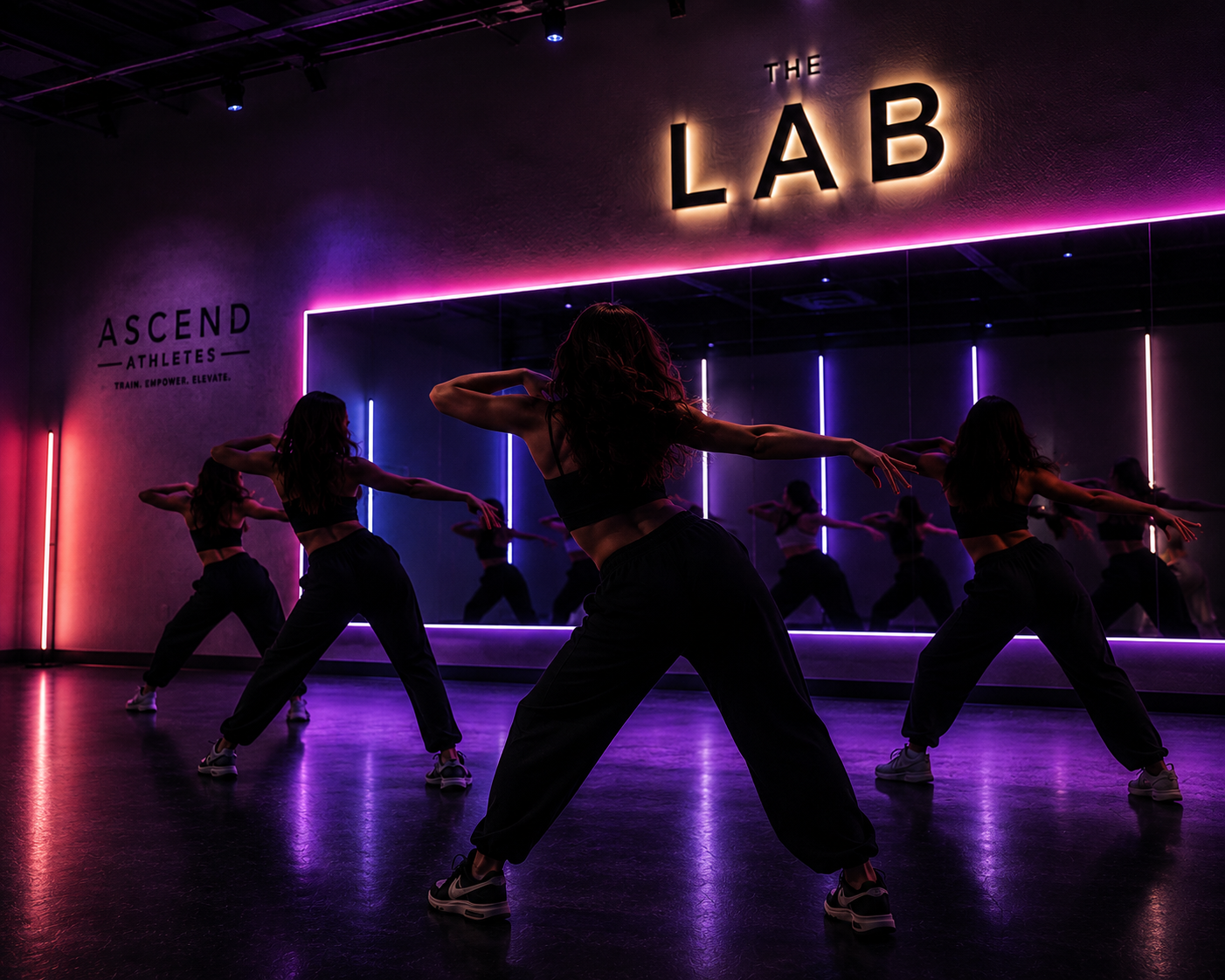 A group of women dancing in a dimly lit dance studio with neon colored lights and a large mirror. The studio has a sign that says "THE LAB" and another that reads "ASCEND ATHLETES TRAIN EMPOWER ELEVATE."