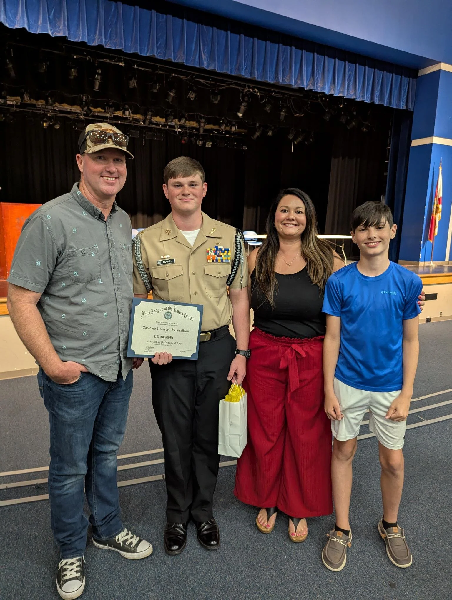 Image with a family of four. Husband, wife, and two sons. Posing with the oldest son with a certificate in hand.