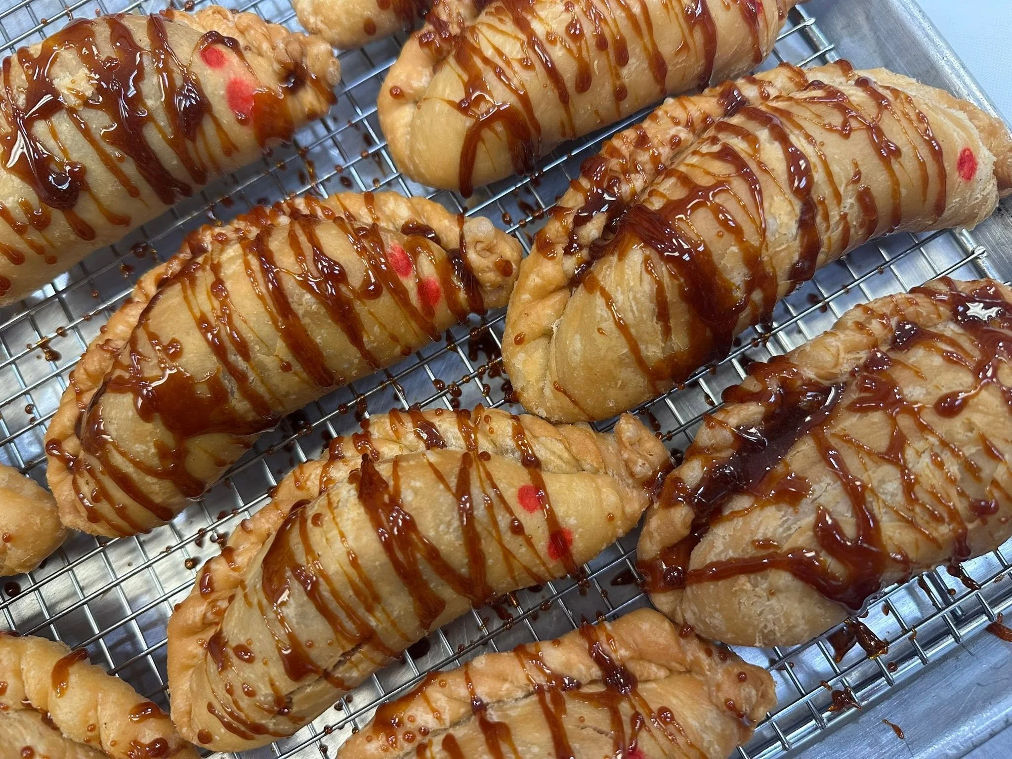 Sweet pastries topped with chocolate drizzle on a wire rack.