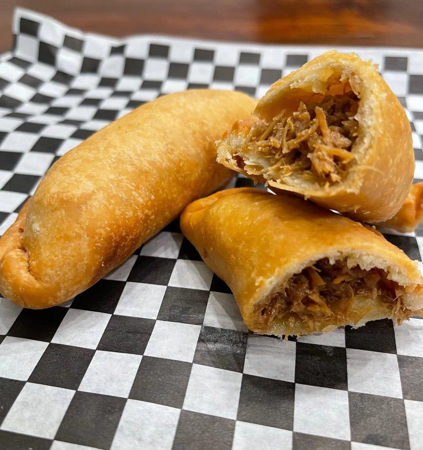 Three egg rolls on checkered paper, one cut open to show shredded meat filling inside.