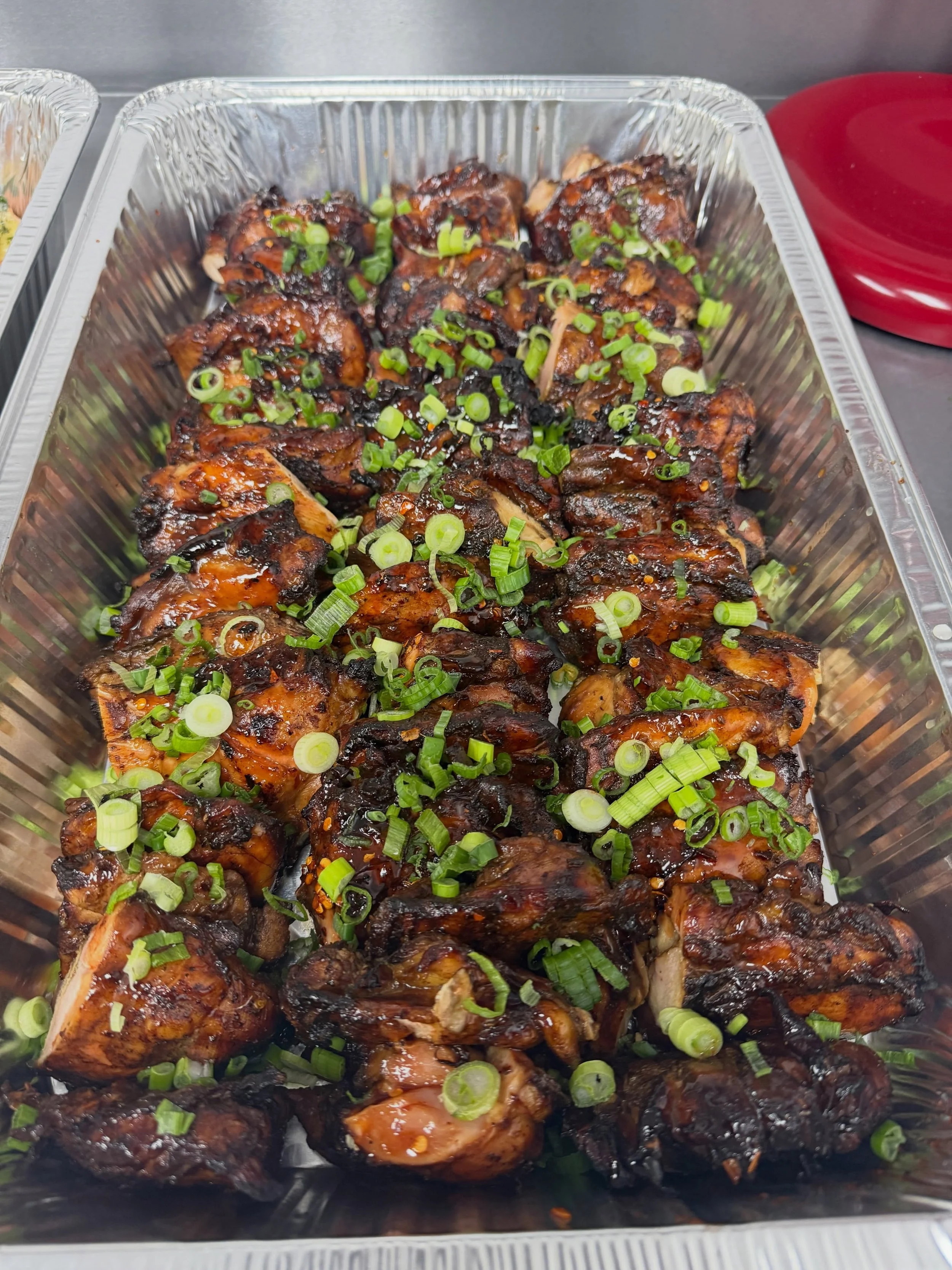 Barbecued chicken drumsticks topped with chopped green onions in a large metallic tray.