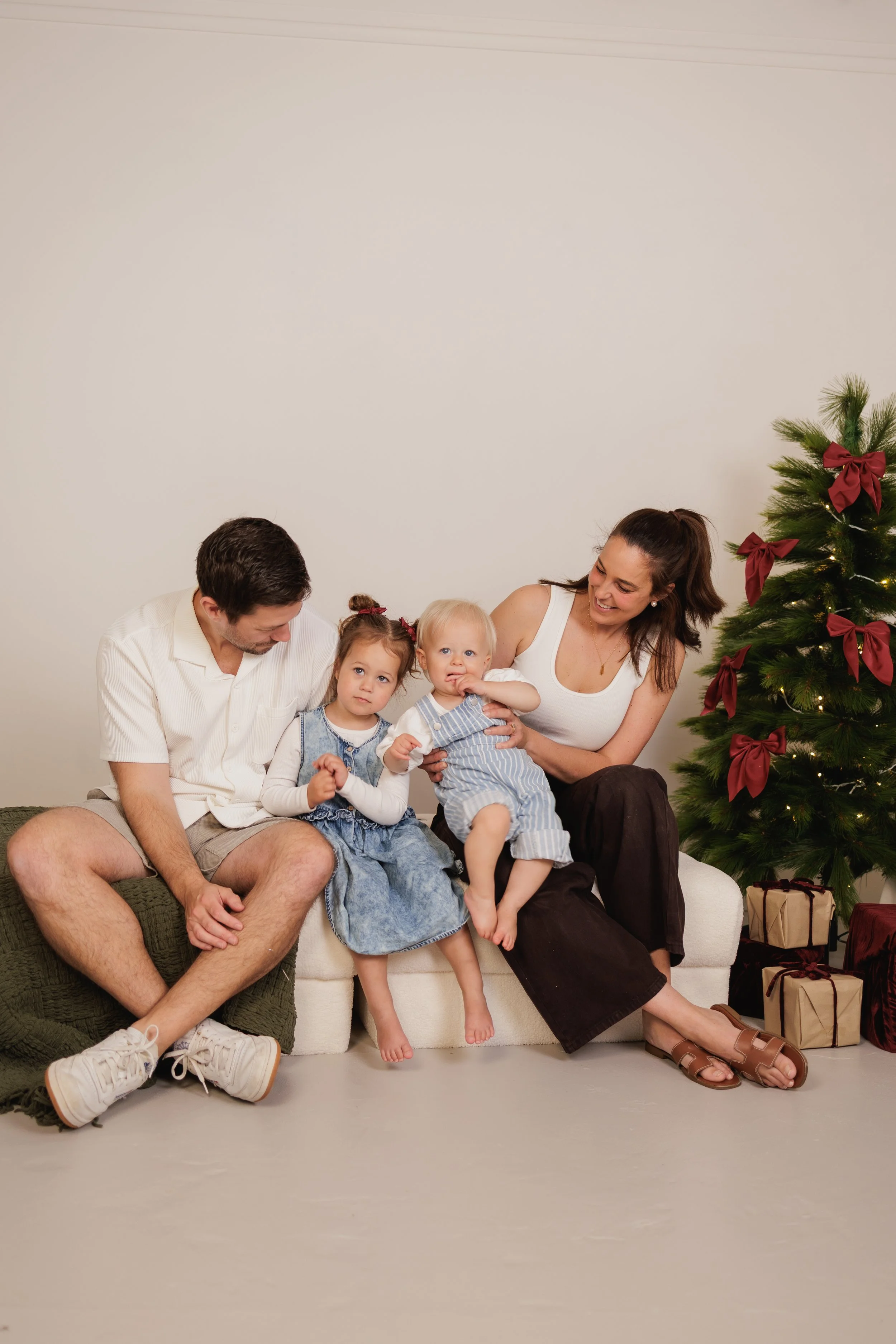 A family sitting together on a couch celebrating Christmas, with a decorated Christmas tree and wrapped presents nearby.