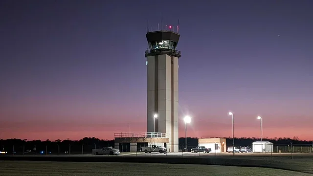 Airport control tower at dusk with parked cars and streetlights