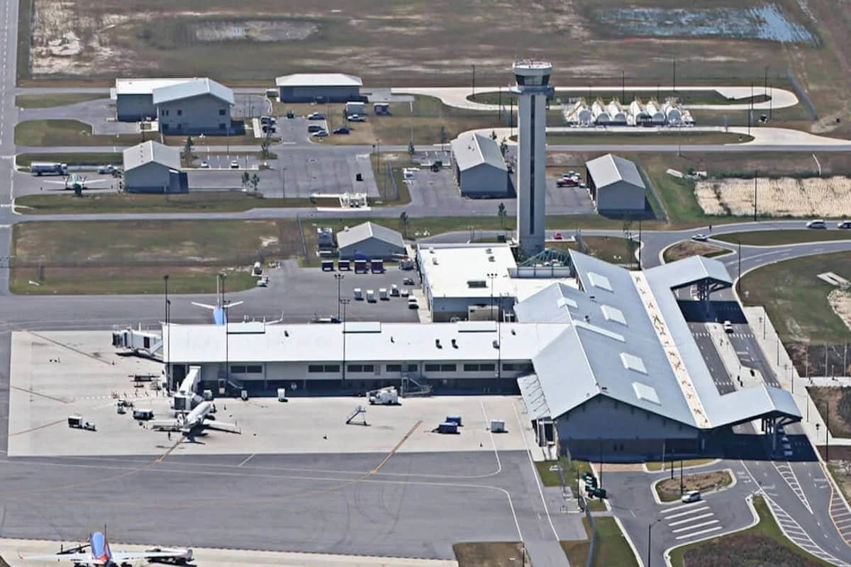 Aerial view of a regional airport terminal with planes on the tarmac, parking lots, roads, and surrounding buildings.