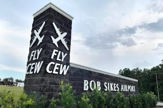 Sign at Bob Sikes Airport featuring flying airplane symbols and the words 'Fly CEW'.