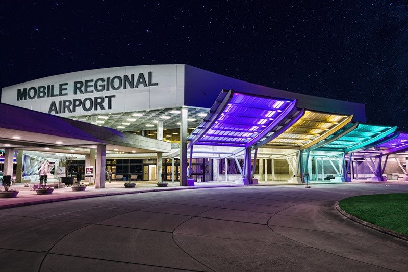 The exterior of Mobile Regional Airport at night with colorful illuminated canopies and a starry sky.