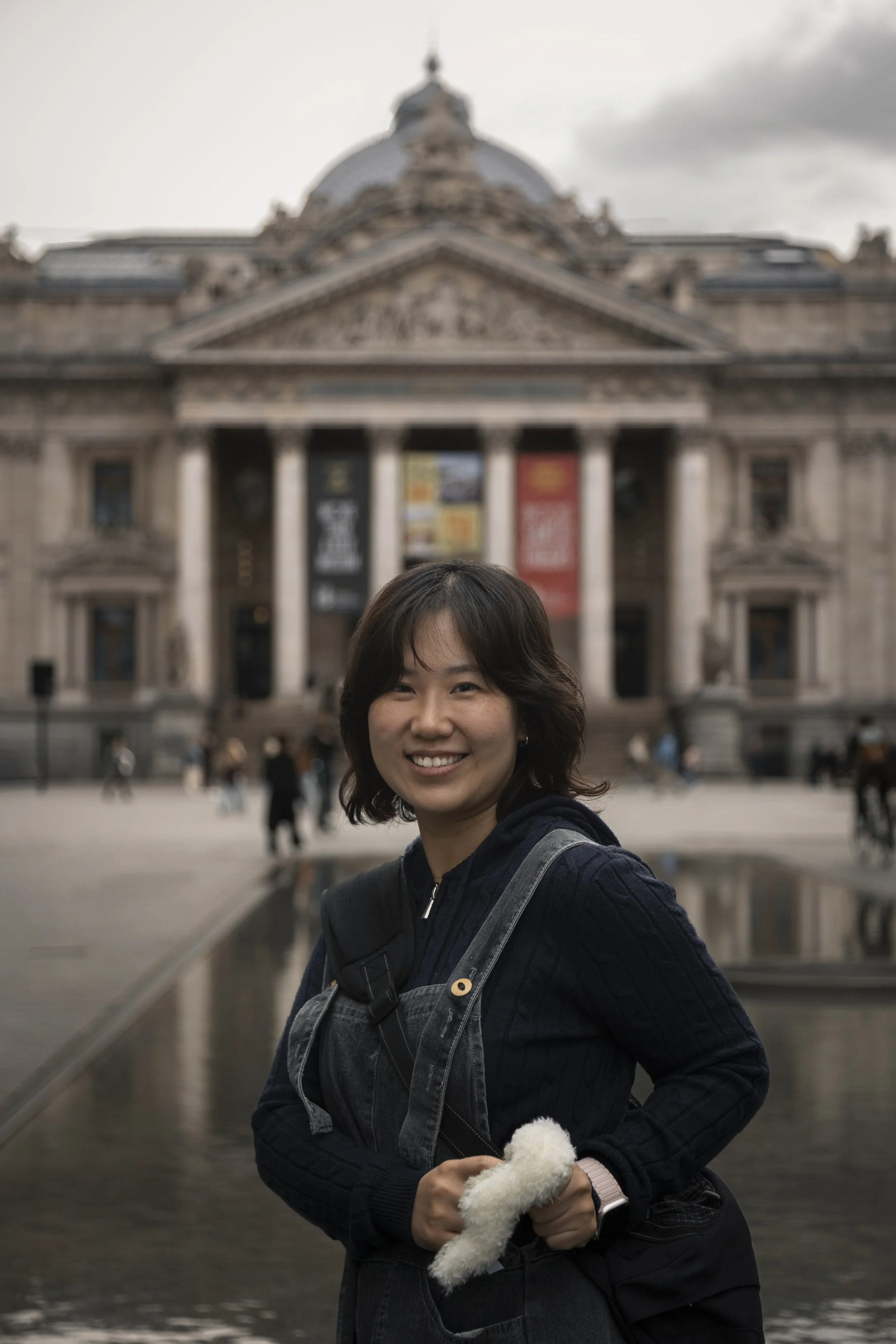A smiling woman standing in front of an ornate historic building, holding a small fluffy white dog.