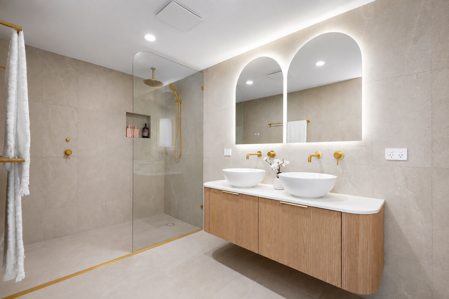 Modern bathroom created by Redlands Bathrooms using our Coastal Luxe Theme, arched mirrors, gold fixtures, LED Lights and dual sink vanity.