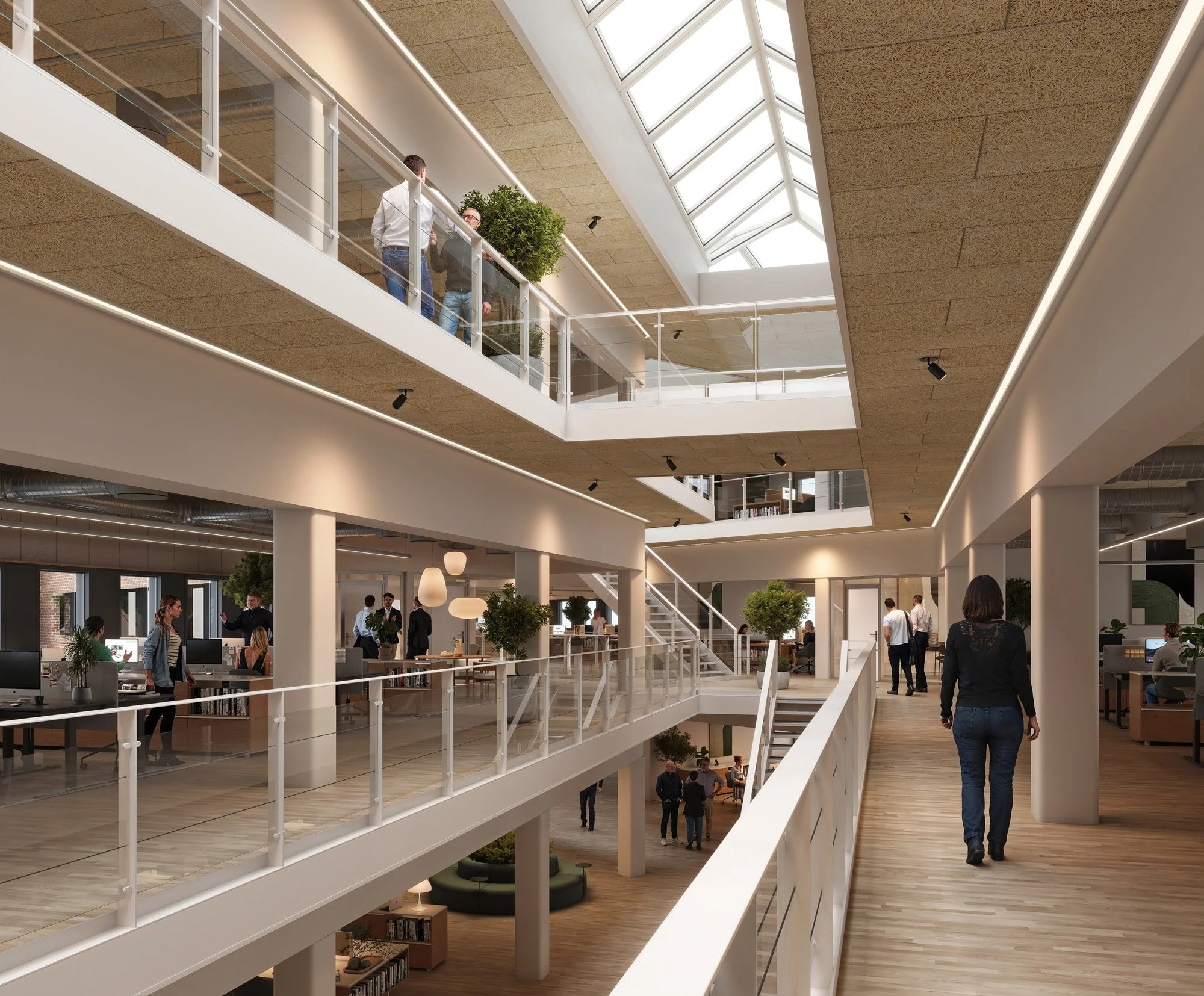 Indendørs billede af et moderne kontorlokale med flere etager, hvor personer arbejder ved computere og går rundt. Loftet har store vinduer, der lader naturligt lys ind, og der er grønne planter i lokalet.