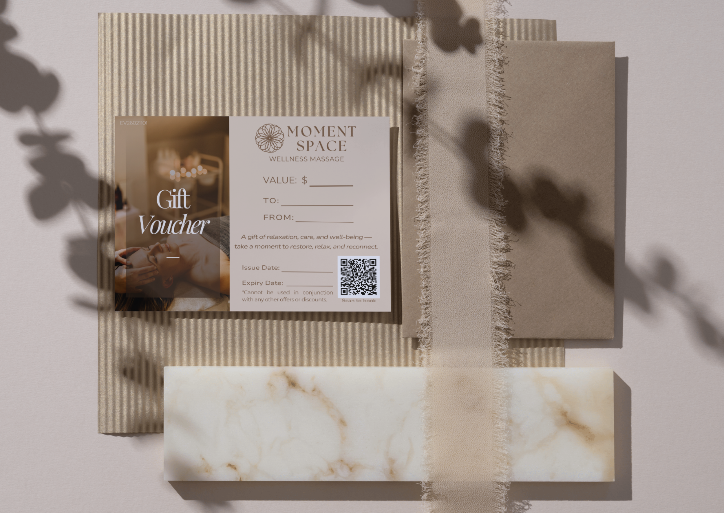 A gift voucher from Moment Space Wellness Massage resting on textured paper and marble patterned samples, with shadows of leaves cast on the background.