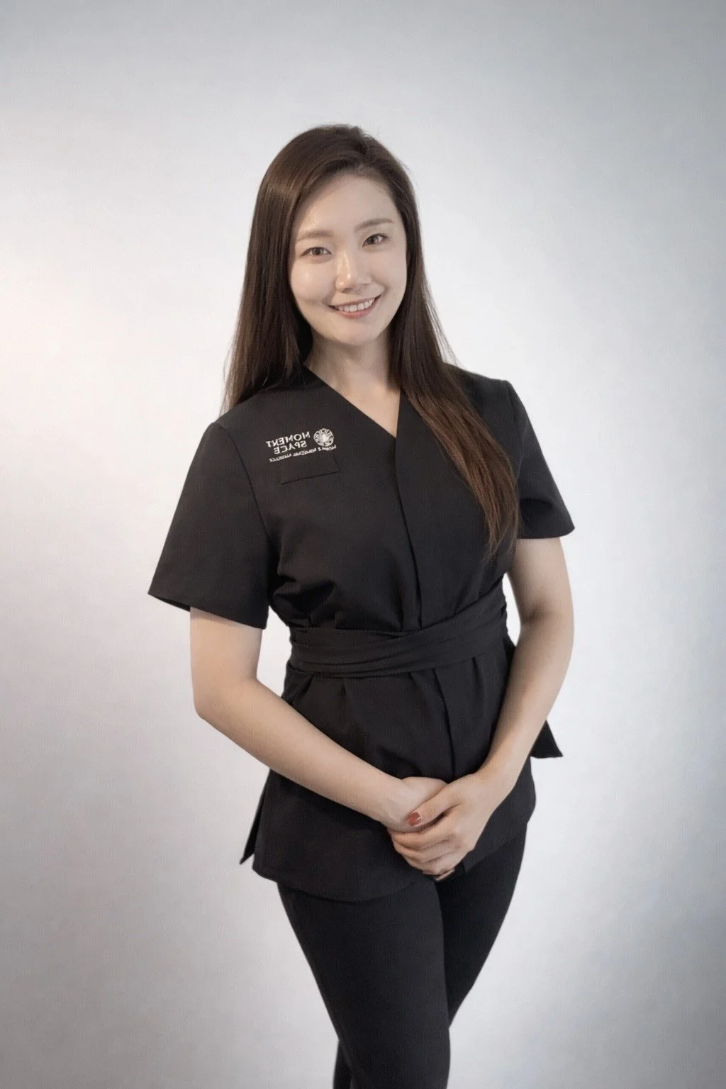 Young woman in black uniform with United Nations and Speech Language Therapy logos, smiling against plain white background.