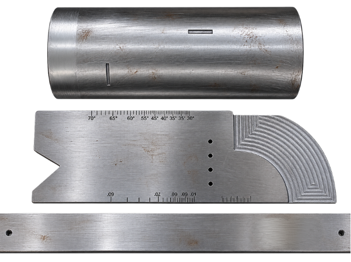 A metal cylindrical object, a stainless steel machinist square with angular markings, and a metal ruler, all placed on a white surface.