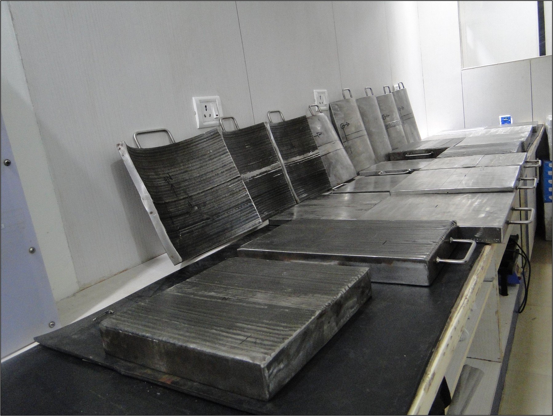 A row of metal molds and templates on a black work surface in a manufacturing or industrial setting.
