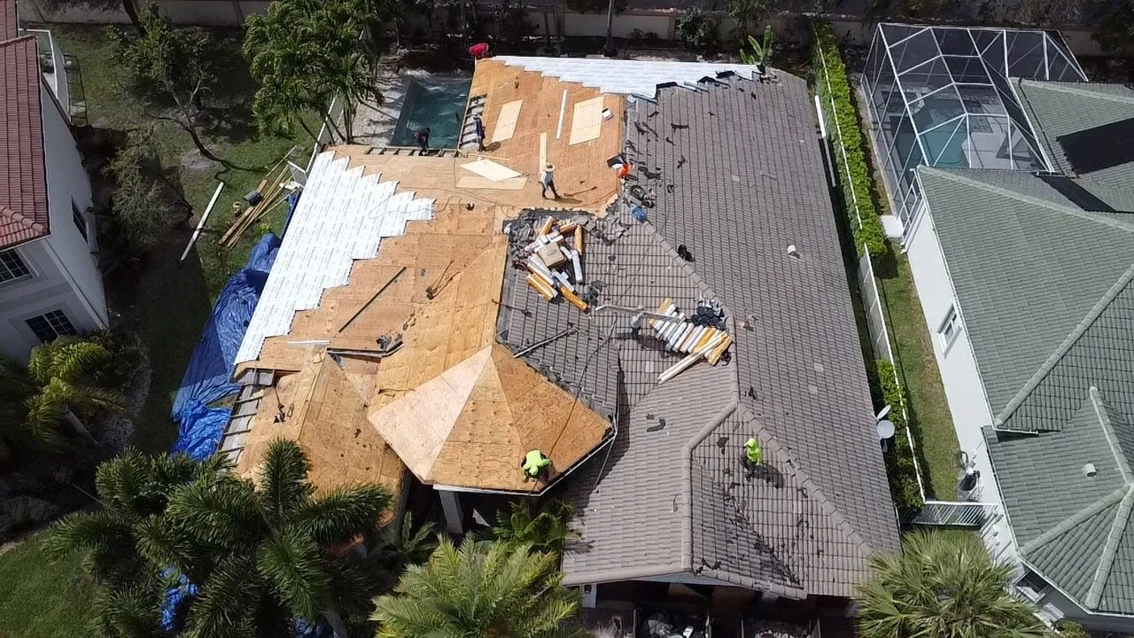 Aerial view of a house roof under renovation with workers and construction materials, including roof tiles and tools.