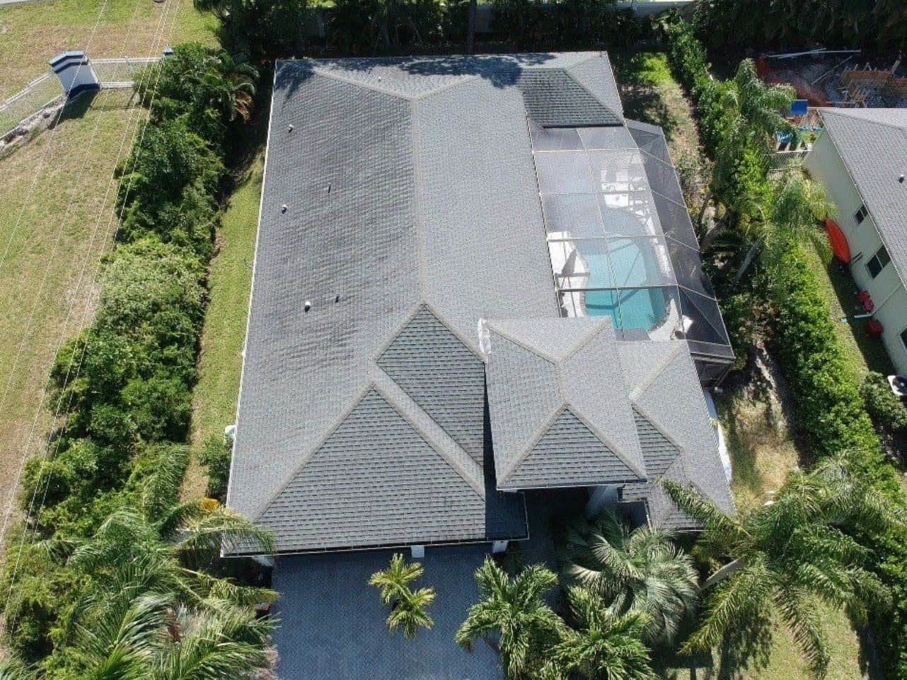 Aerial view of a large house with a screened-in pool, surrounded by greenery and palm trees.