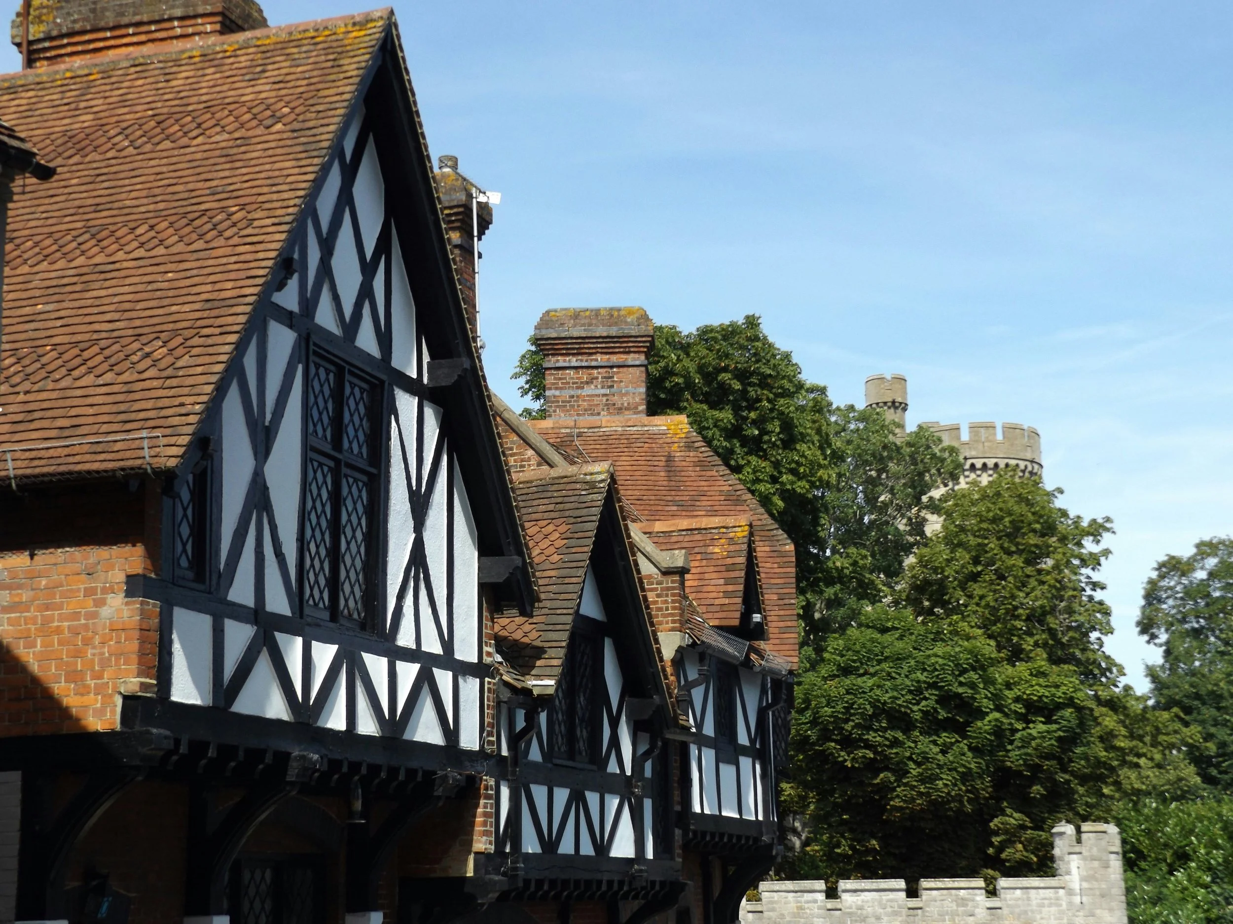 A row of traditional Tudor style houses with black and white timber framing and red brick chimney stacks under a clear blue sky.