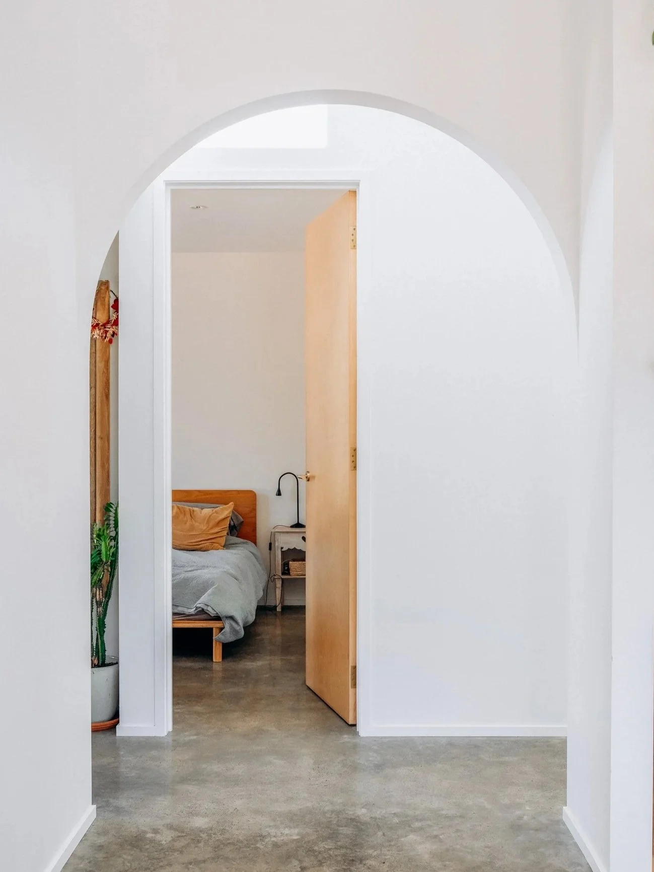 View through an arched doorway into a bedroom with a bed, nightstand, and a lamp.