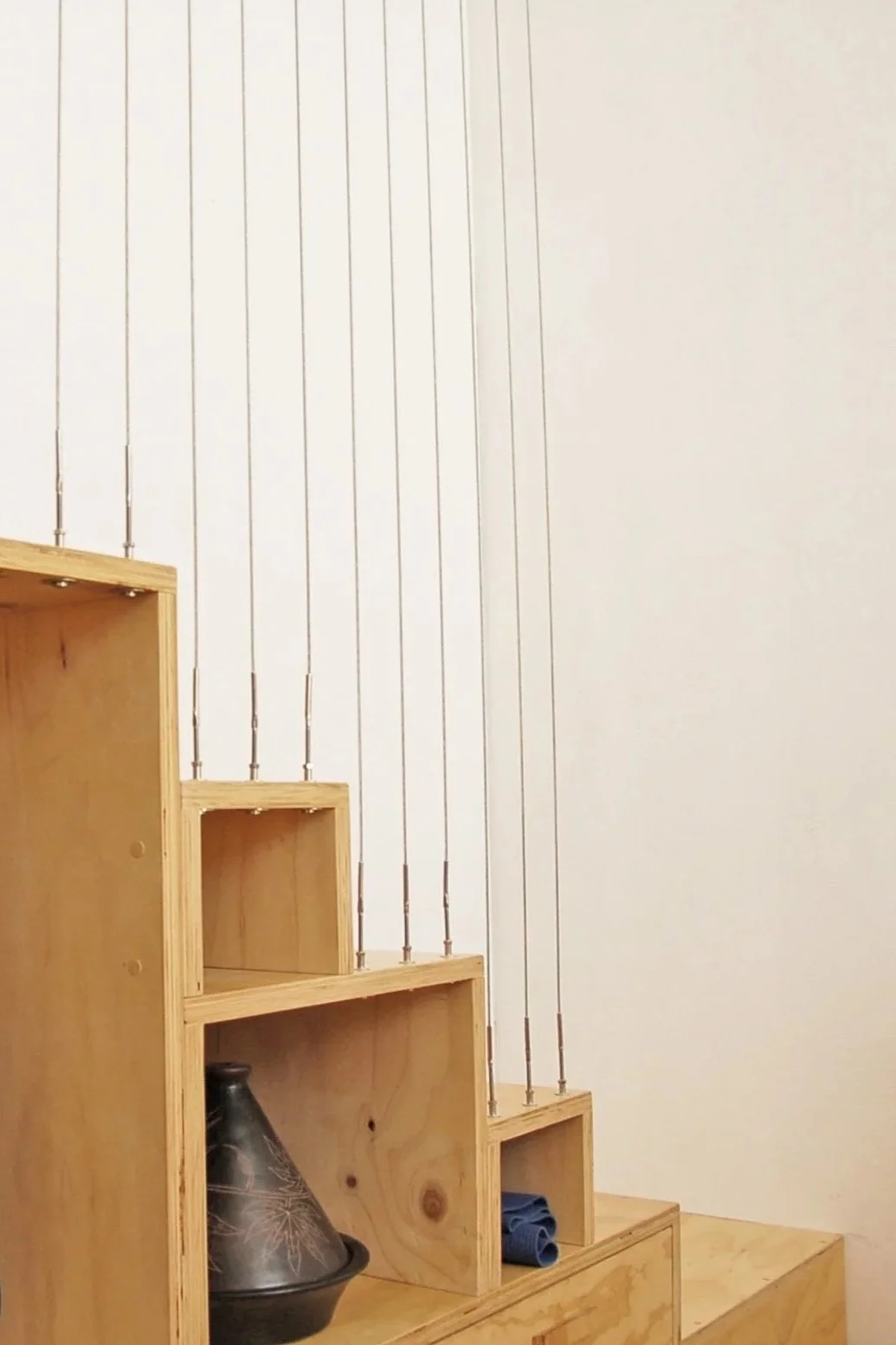 Wooden staircase with several open compartments, next to a plain white wall with vertical black metal rods.