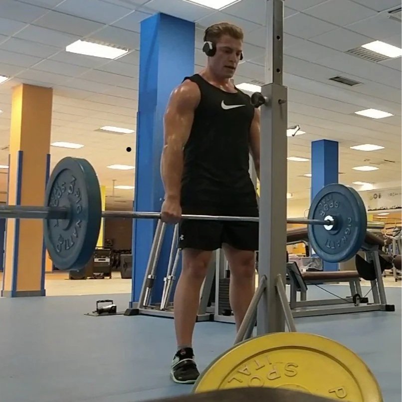 Uomo che solleva un bilanciere in palestra, indossa cuffie e abbigliamento sportivo nero.