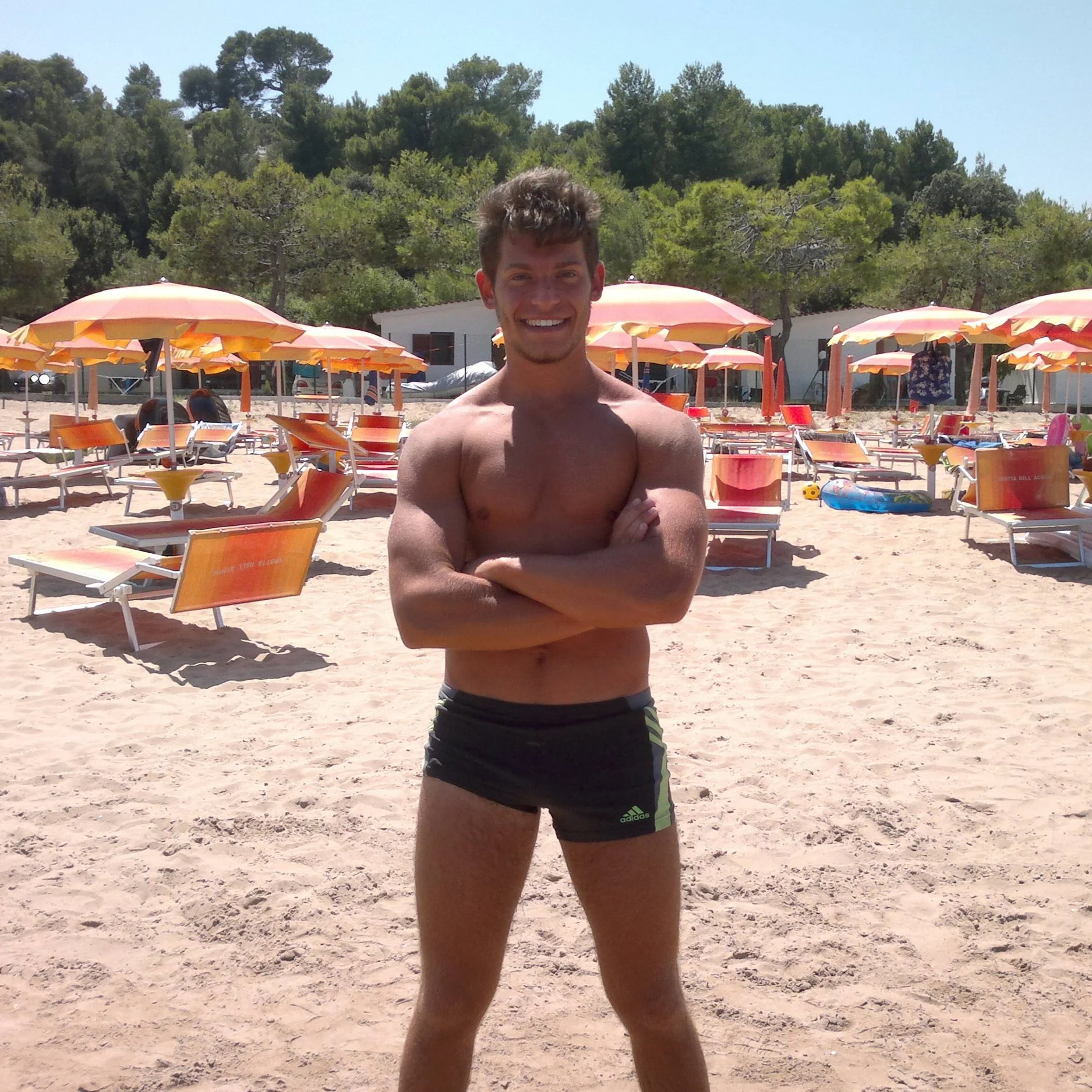 Un giovane prende il sole sulla spiaggia con ombrelloni arancioni e sdraio.