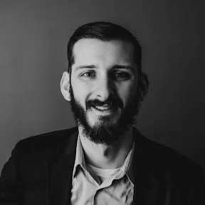 Black and white portrait of a man with a beard, smiling and wearing a blazer and shirt