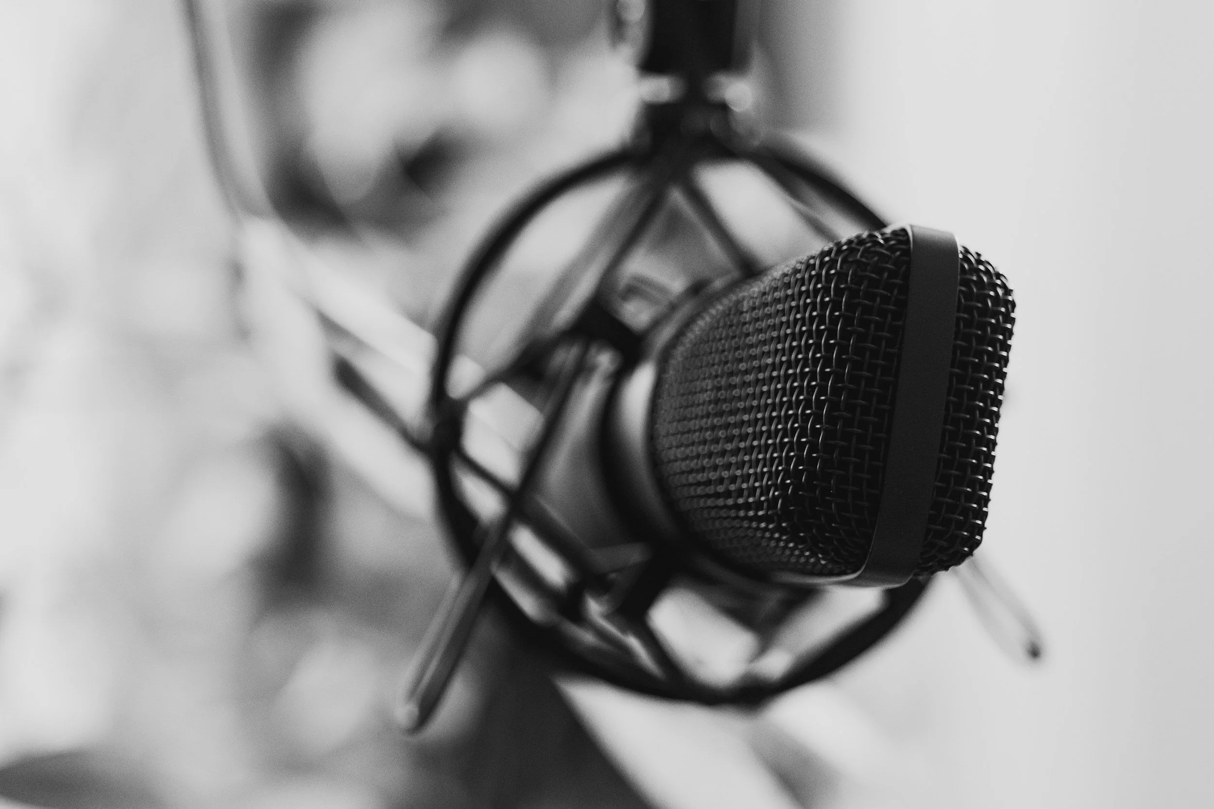 Black and white close-up of a microphone with a person blurred in the background.