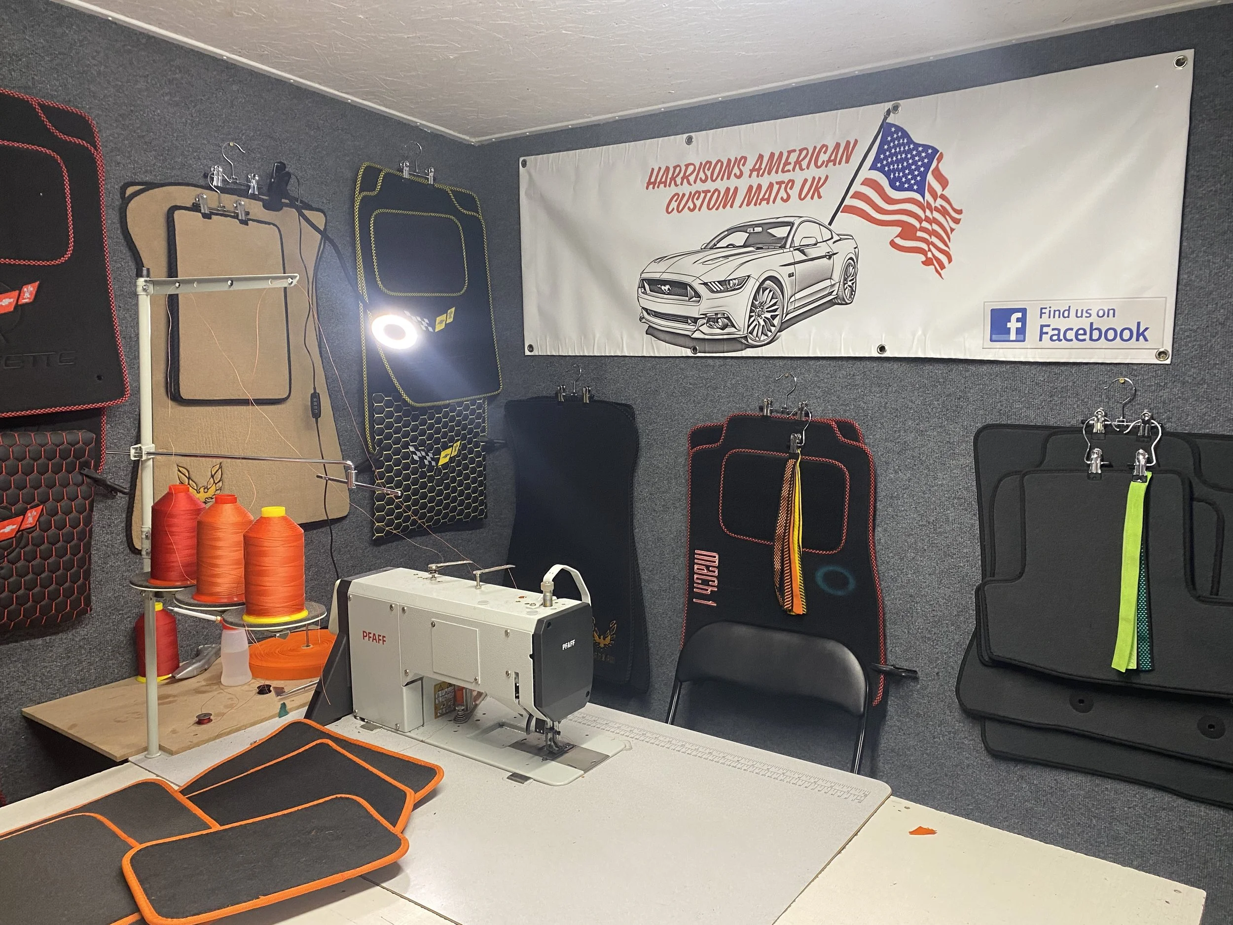 Workshop display with car mats hanging on the wall, some quilting or sewing tools, a sewing machine, and foam mats on the table for assembly or work.