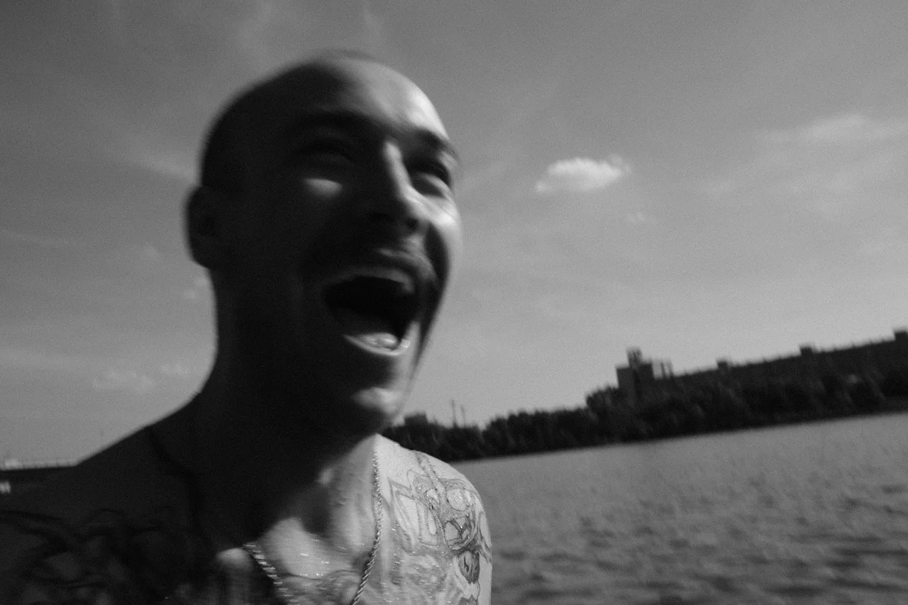 Lächelnder Mann mit tattoos am Meer bei Sonnenuntergang, Schwarz-Weiß-Foto.