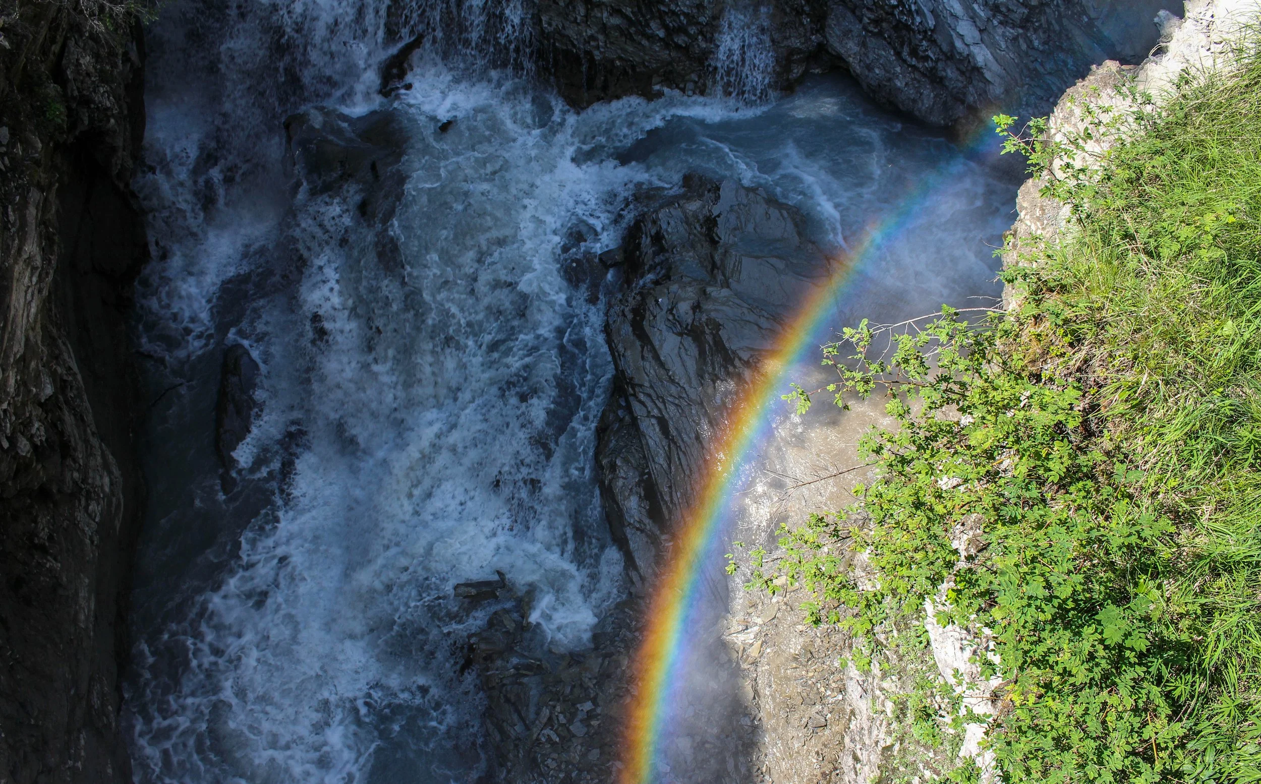 Wasserfall mit Regenbogen zwischen Felsen und Bäumen