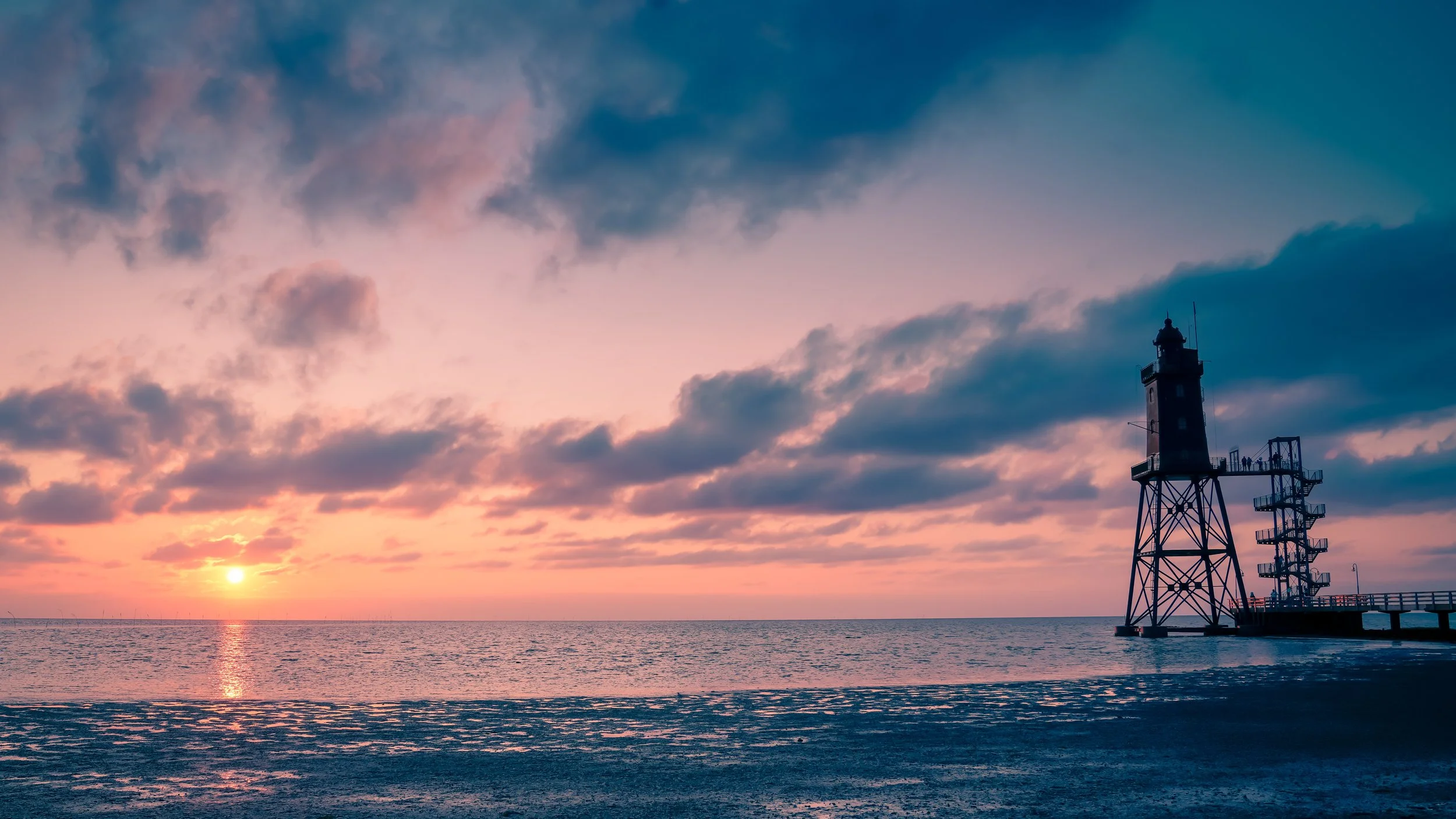Leuchtturm im Wattenmeer bei stimmungsvollem Sonnenuntergang