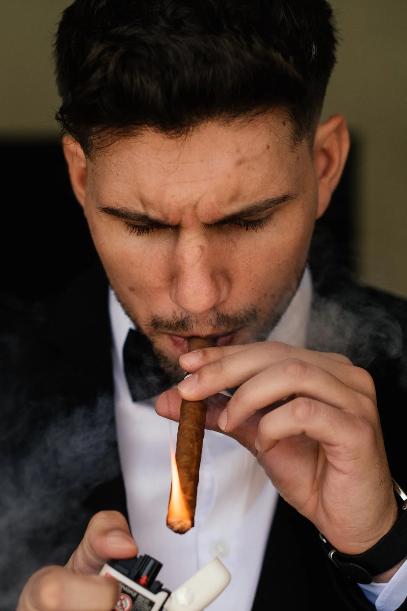 A young man in a suit and bow tie is lighting a cigar with a lighter.