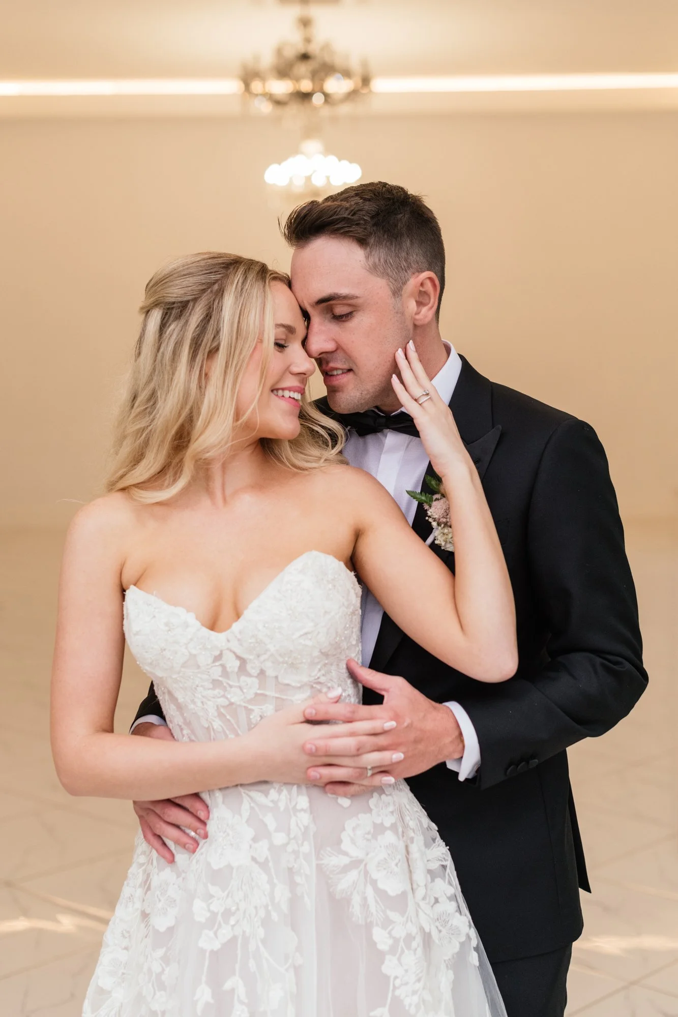 The bride and groom moments before their wedding reception enjoying their relaxed couple shoot.  The bride is wearing a white lace wedding gown and the groom is in a black tuxedo with a bow tie.