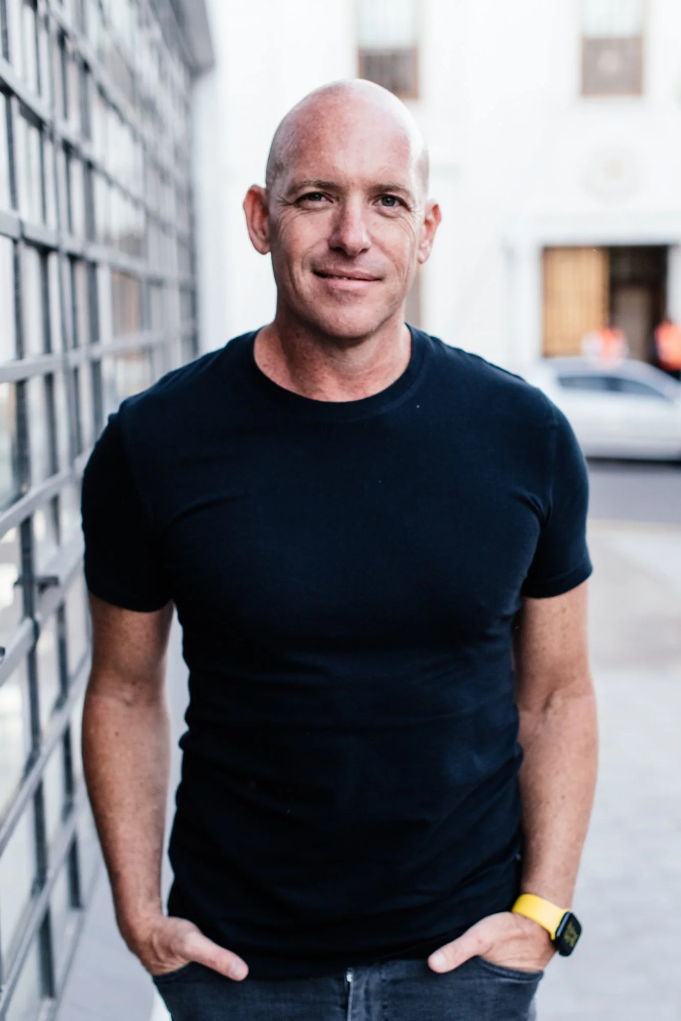 Darren Bester wearing a black T-shirt standing outdoors in front of a building with windows.