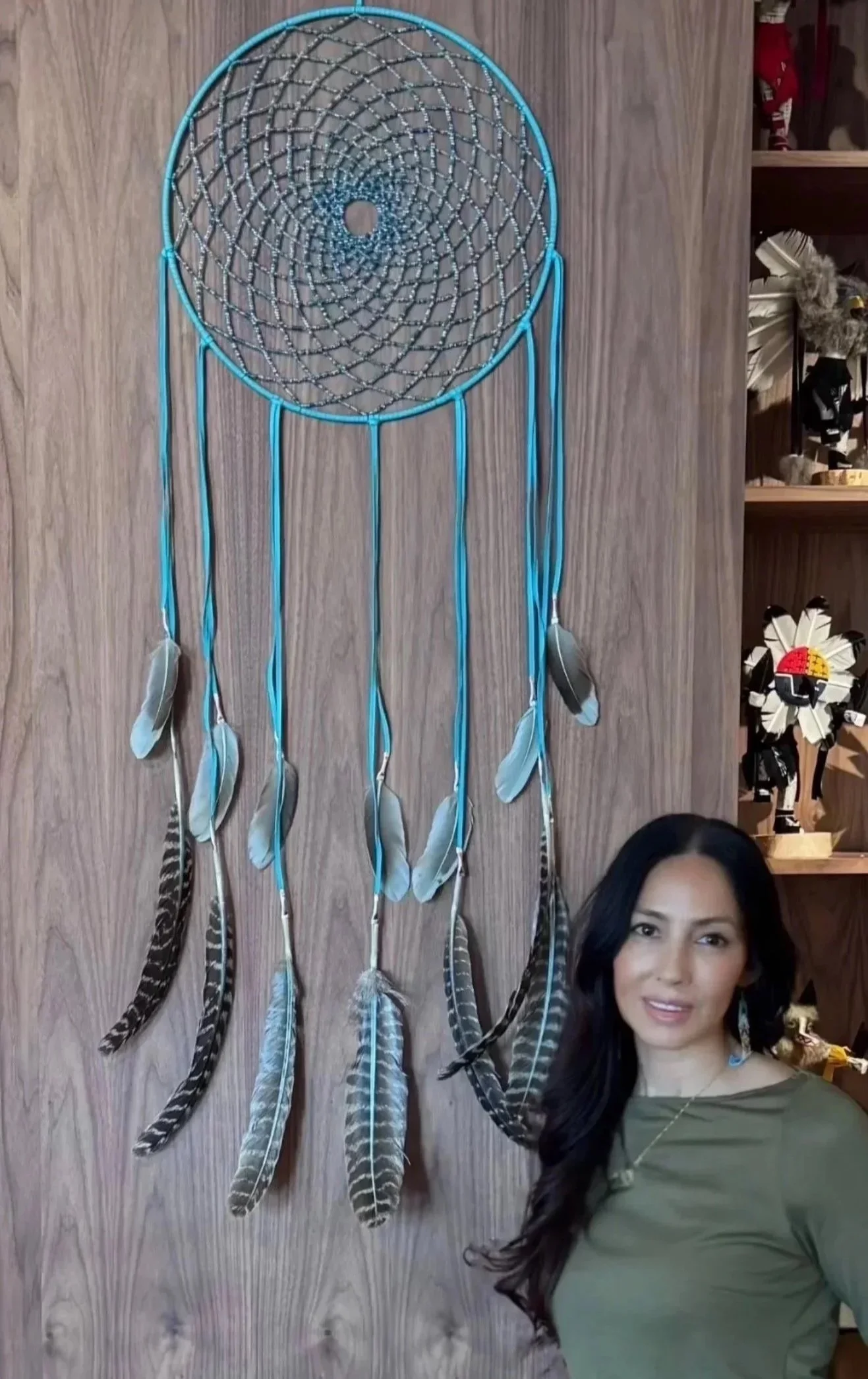 Cheryl Shenandoah standing beside an original handcrafted Haudenosaunee dreamcatcher.