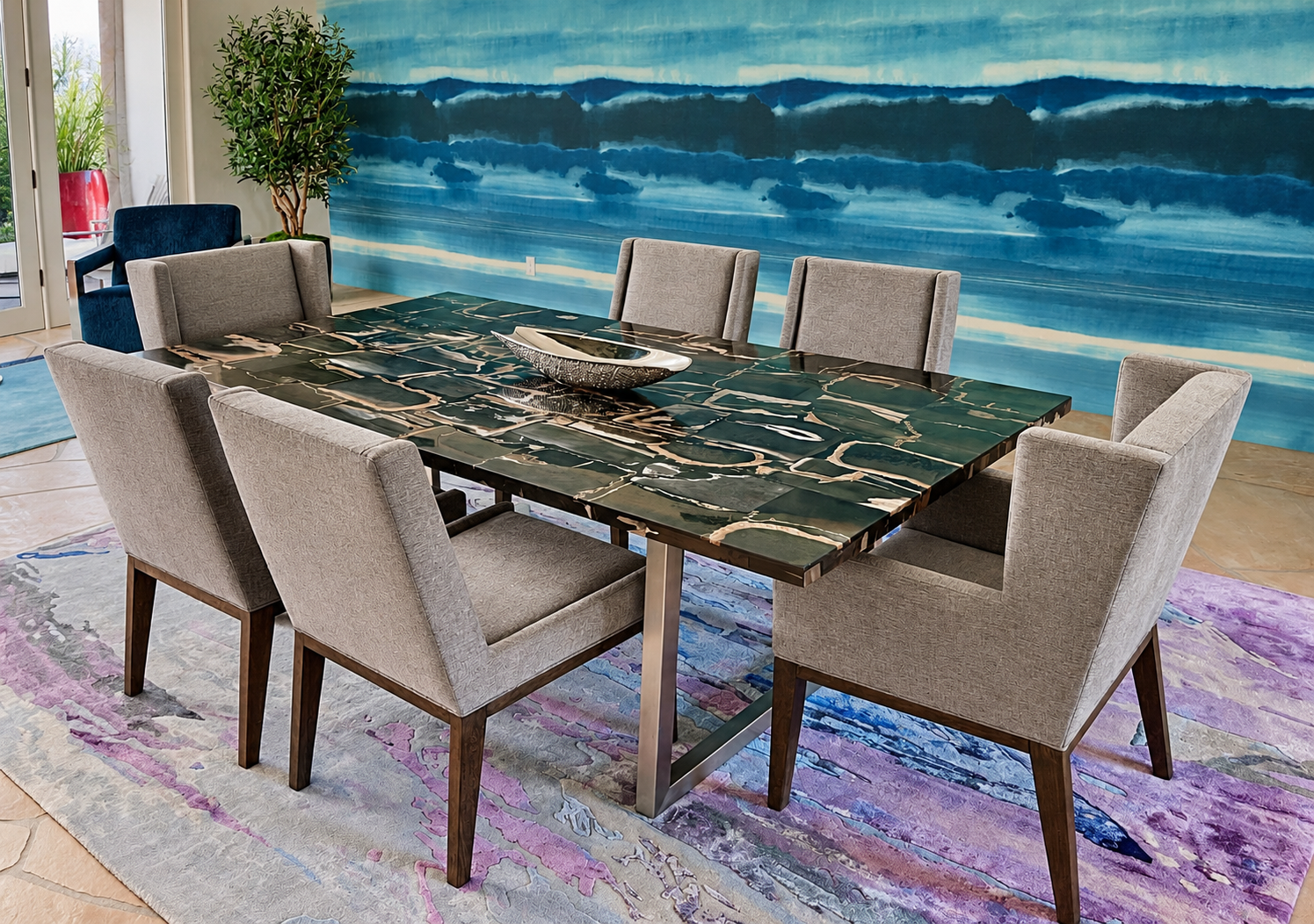 A dining room with a modern black marble table surrounded by eight light grey upholstered chairs. The room features a large, abstract blue wall mural, a potted plant, a glass door, and a colorful area rug.