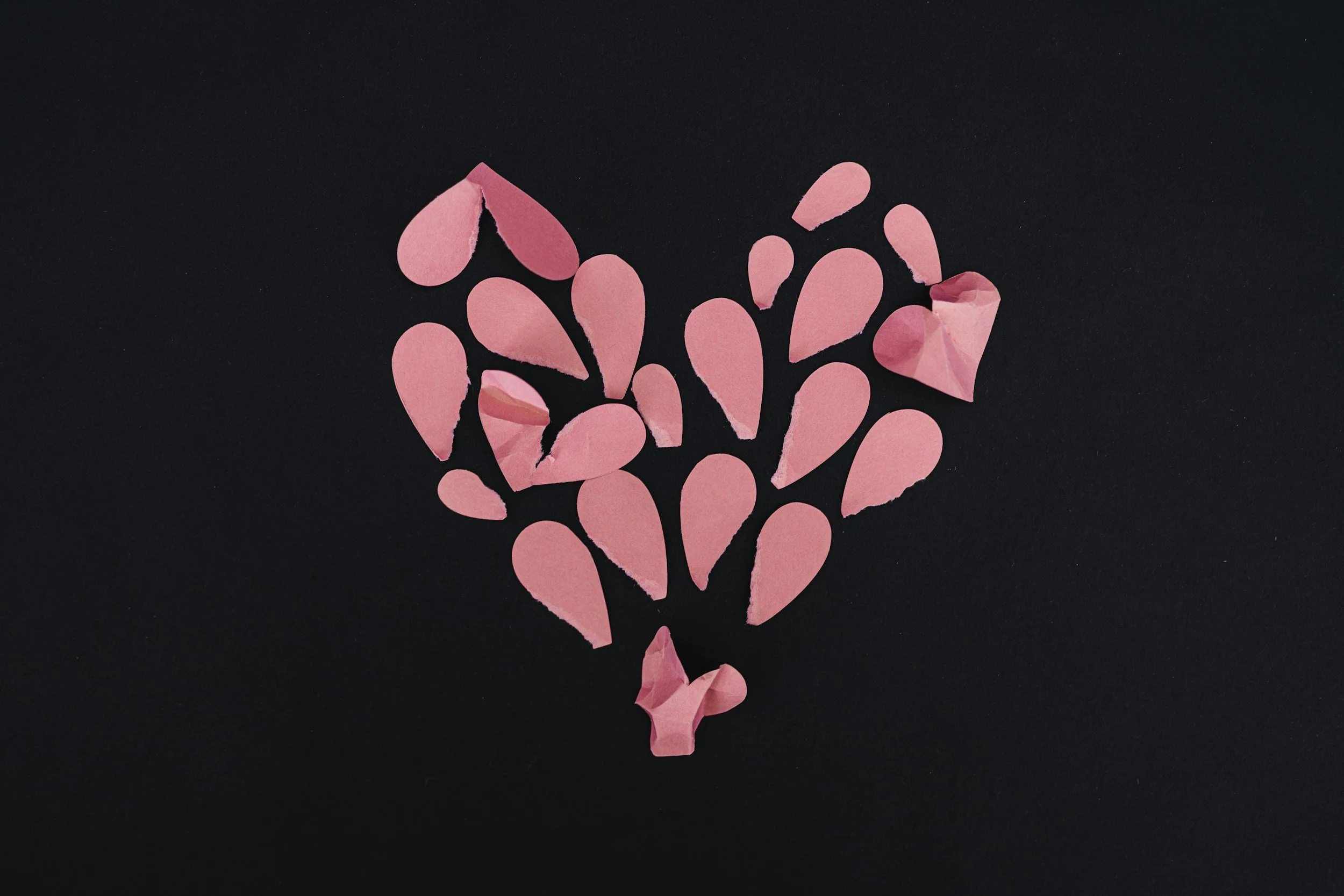 Découpage de cœurs en papier rose formant un bouquet contre un fond noir.