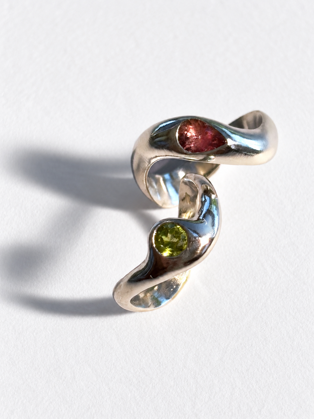 Bague en argent 925 avec deux pierres précieuses, l'une rose et l'autre verte, sur un fond blanc. bijoux contemporains aux lignes organiques.