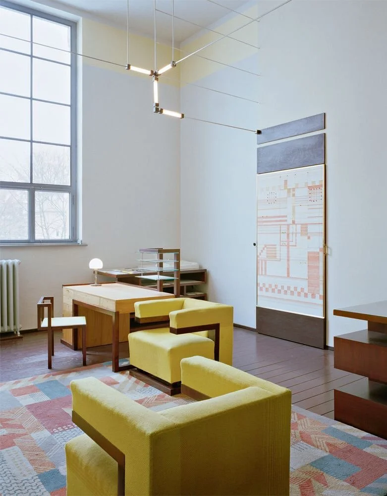 Salon moderne avec fauteuils jaunes, bureau, grand tableau mural, grande fenêtre, lampe de bureau et décor minimaliste.