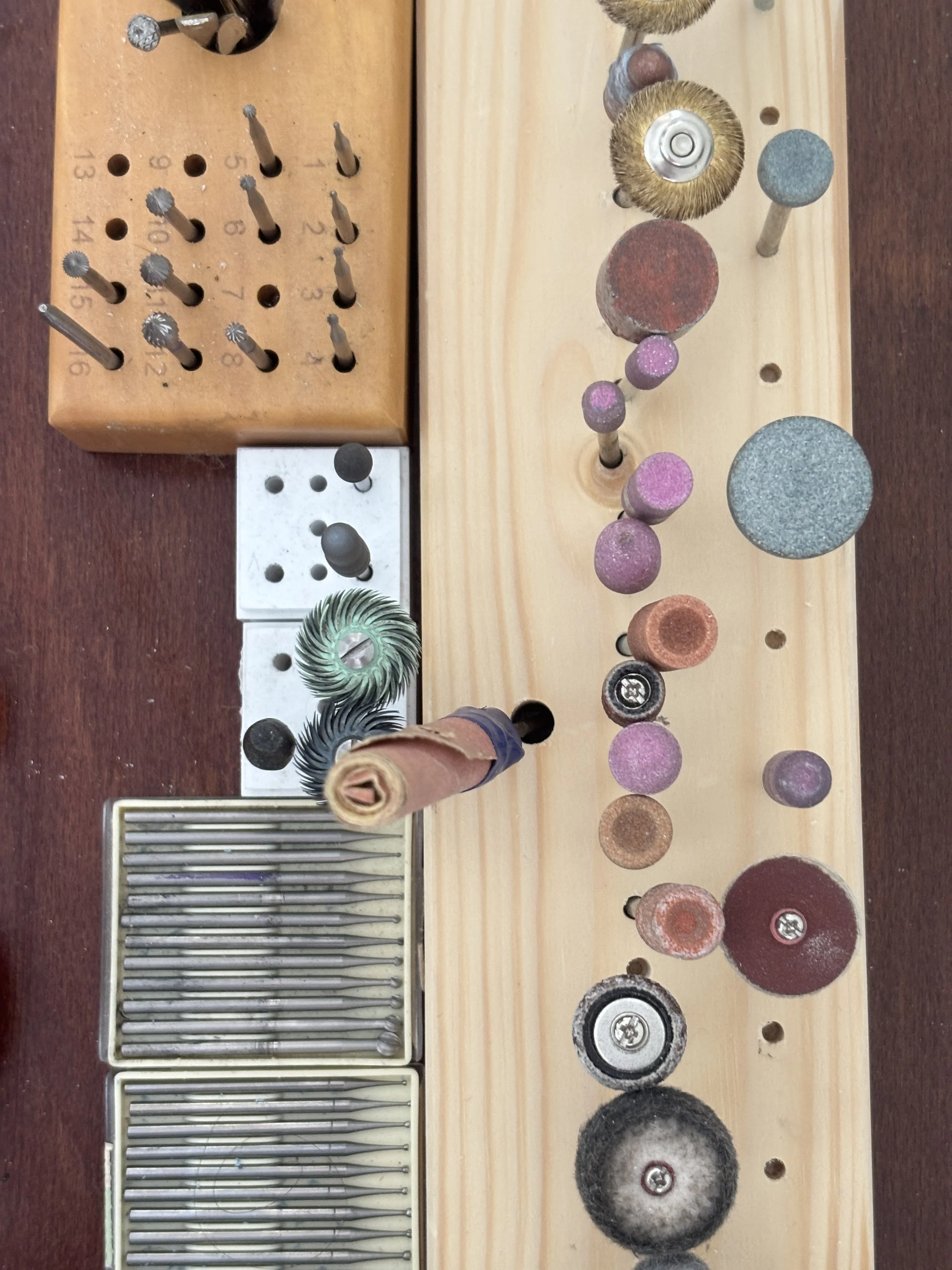Une planche en bois avec différents outils abrasifs, meules, brosses, et drills de différentes tailles et textures, utilisés pour le polissage, le brasage, la fonte, l'émerisage ou la finition de surfaces.