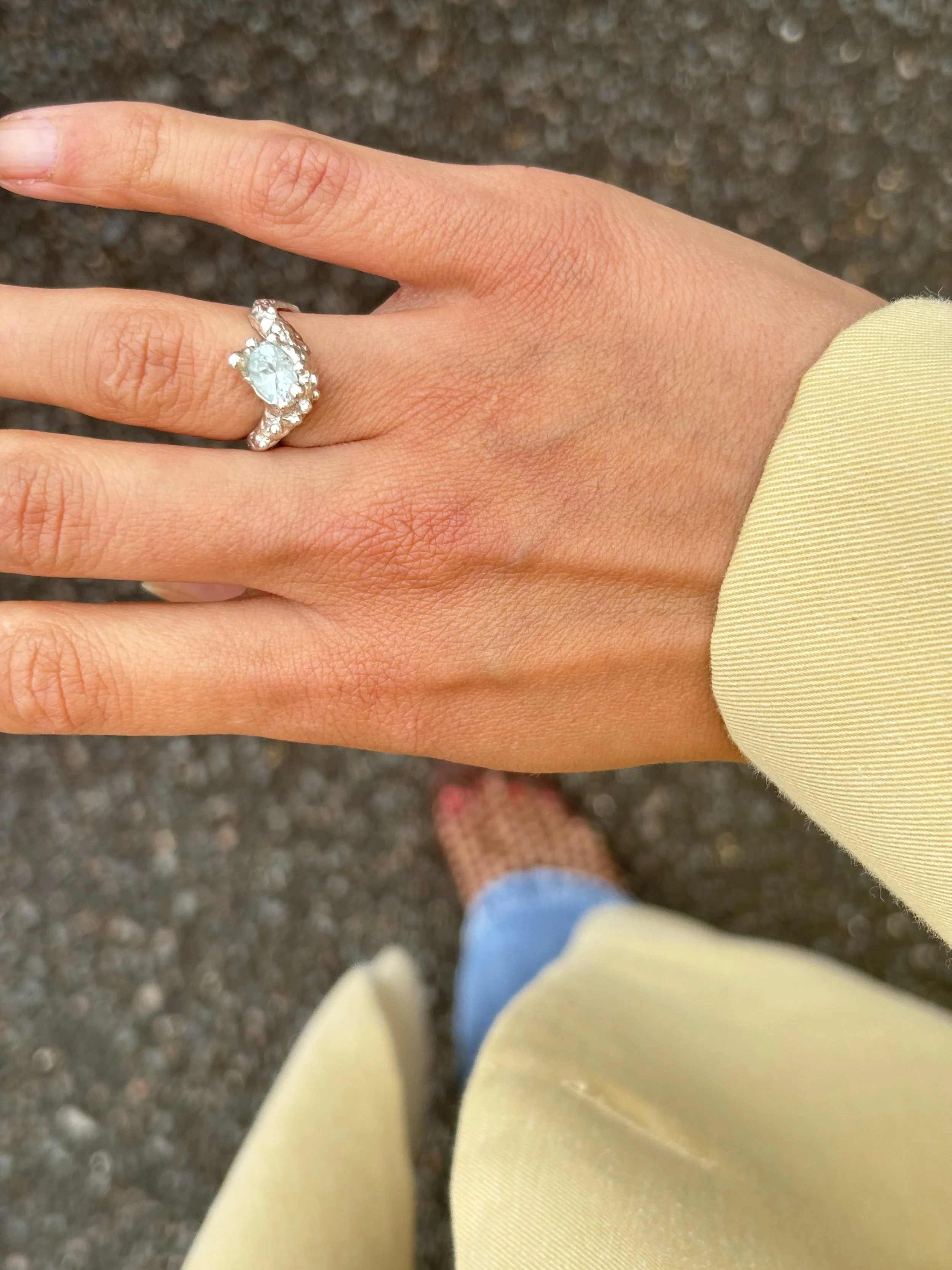 Une main portant une bague avec une pierre précieuse portée quotidiennement pour une promenade en ville, un style résolument féminin et élégant.
