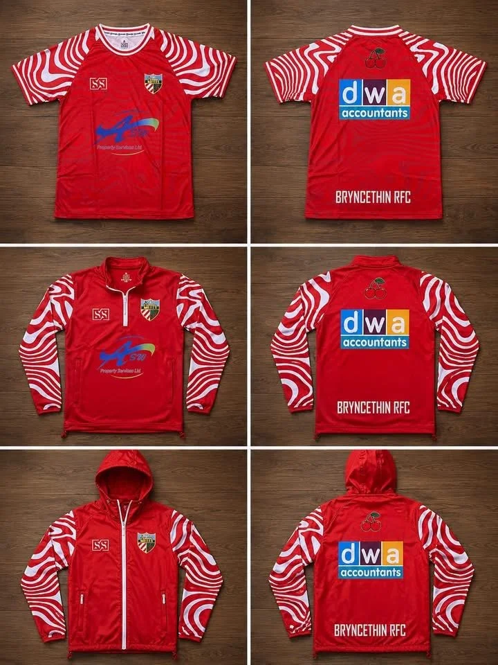 A red athletic tracksuit with white and red patterned sleeves and the Baden County crest, featuring a cherry logo on the front and a large DW Accountants logo on the back. The set includes a short-sleeve shirt, a long-sleeve shirt, and a hooded jacket.