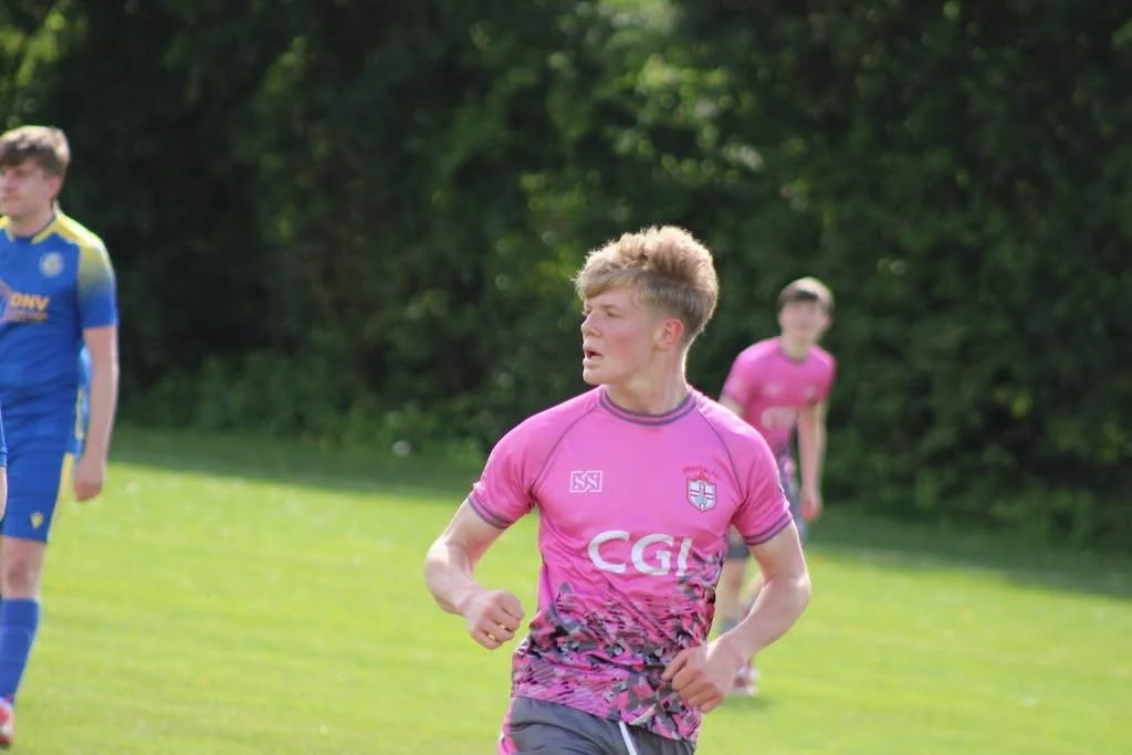 Young male soccer player wearing a pink jersey running on a grassy field during a game.