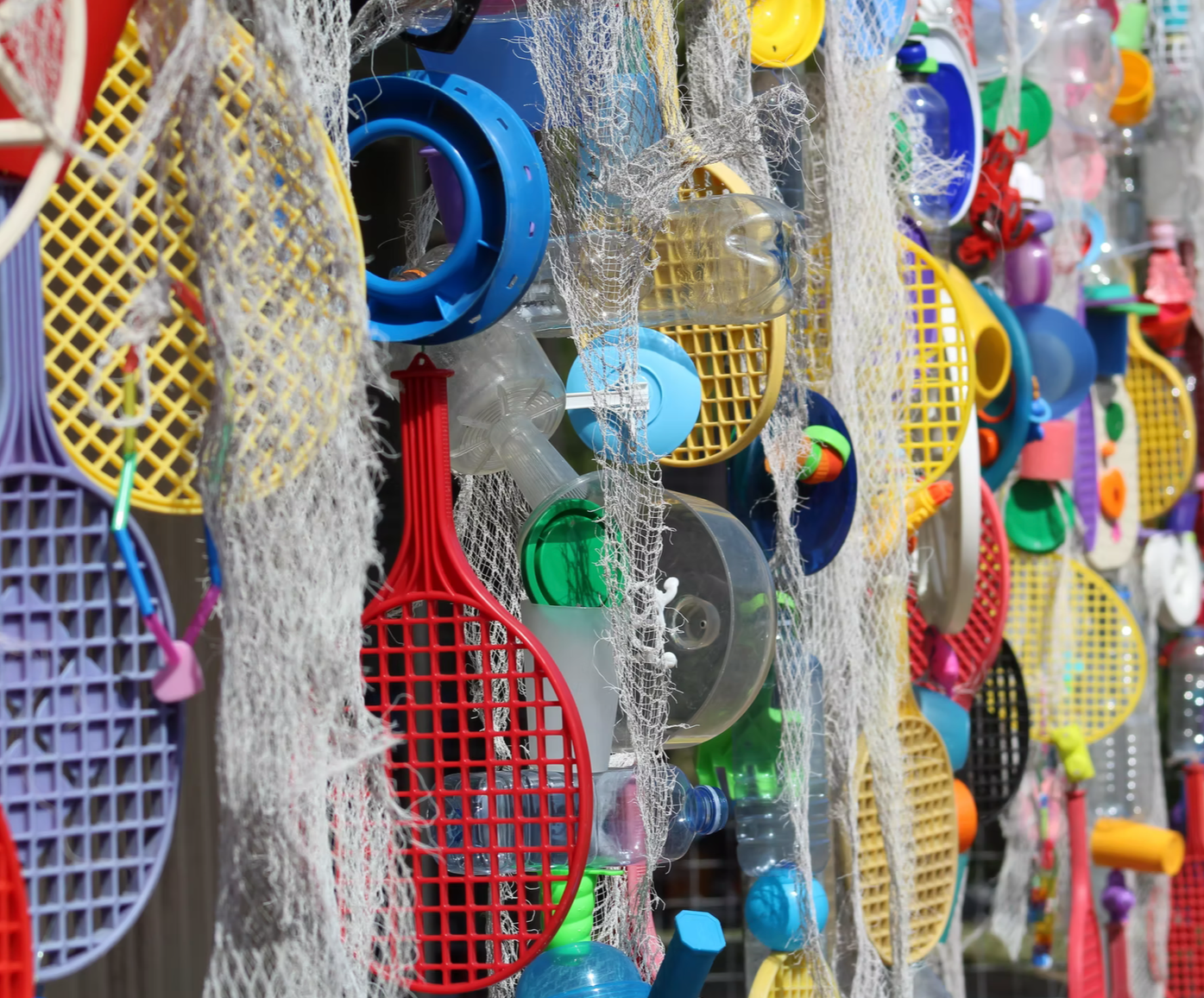 Colorful plastic toy tennis rackets, balls, and other small beach toys hanging on a display with some fishing nets.