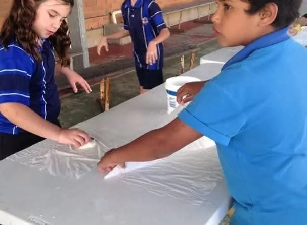 Children are participating in a school based lantern workshop. They are applying glue to the paper.