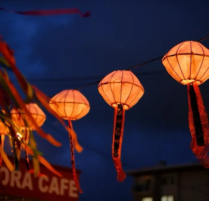 String of glowing orange paper lanterns hanging against a dark evening sky at night.